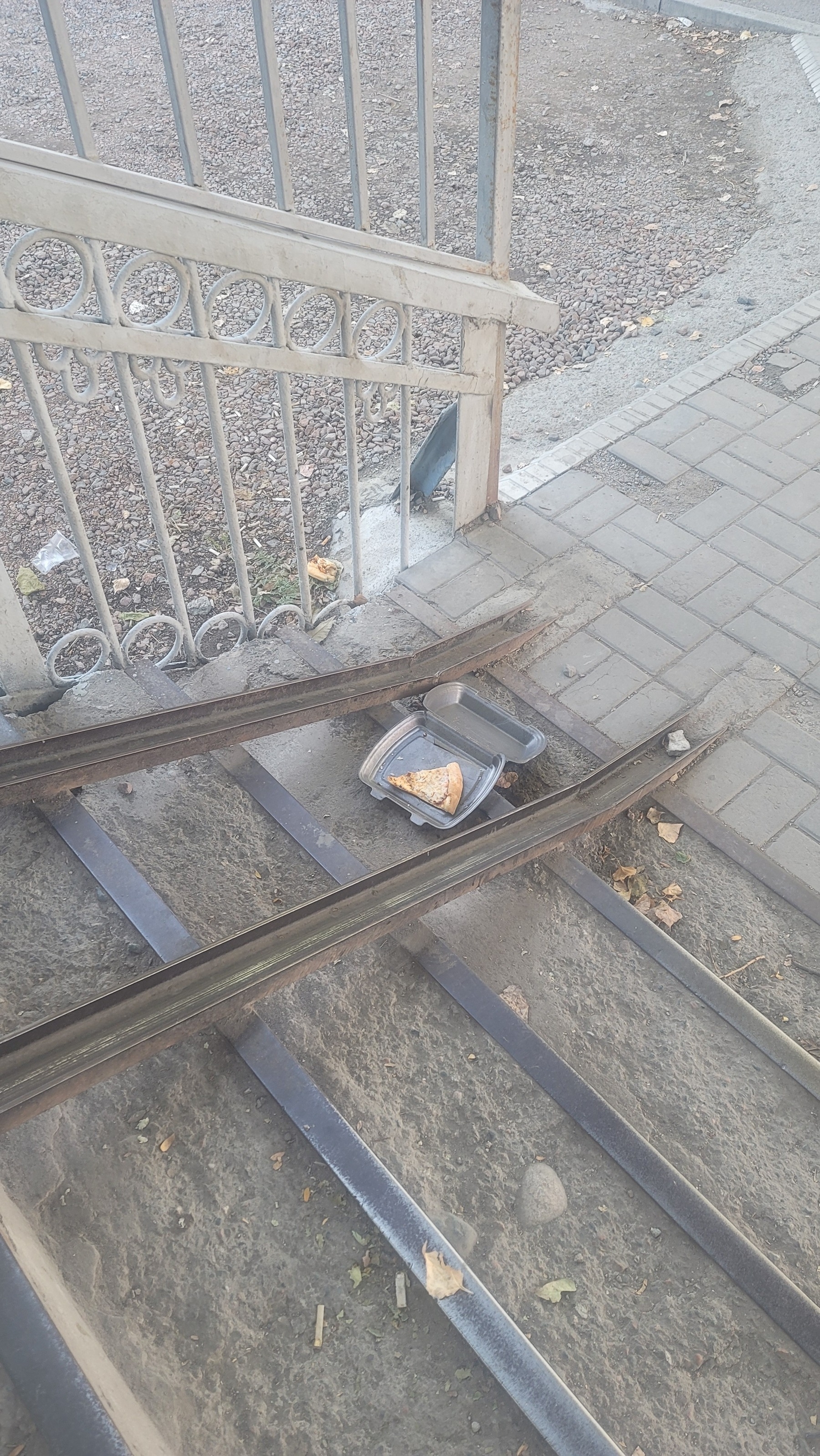 slice of pizza in a black, styrofoam to-go box without a top, left on the first step of an outdoor stairwell