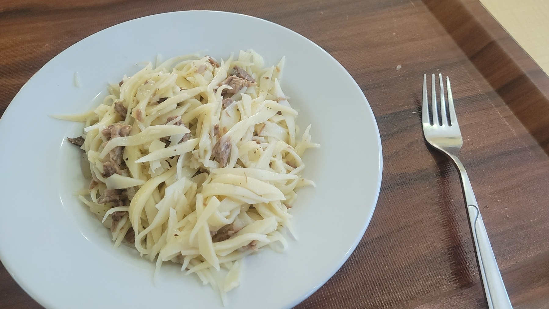 beshbarmak on a plate on a brown cafeteria tray with a fork to the right