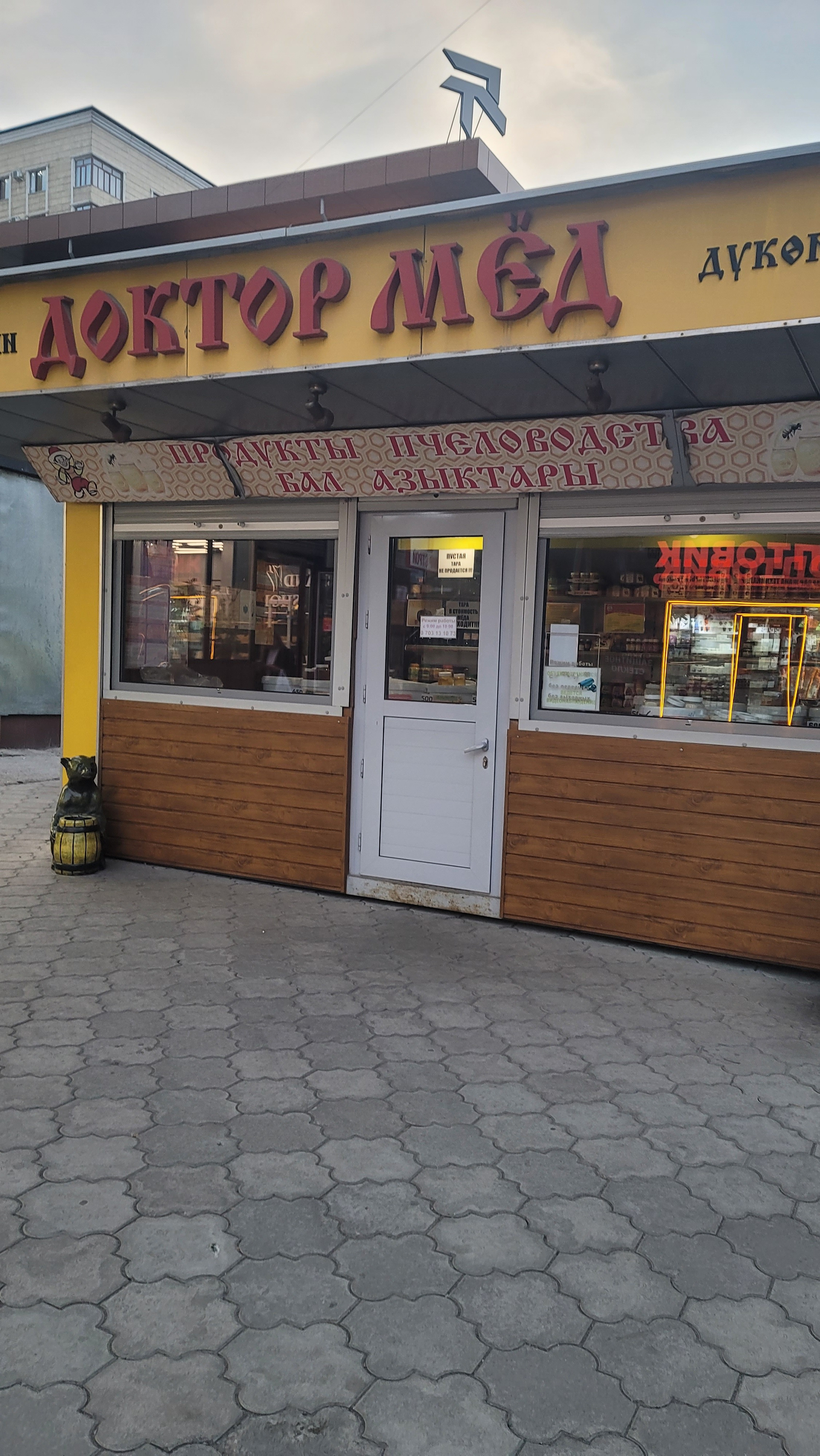 Small yellow shop with the name Доктор мёд (Doctor Honey) in red letters. One big window on each side of the door, through which you can see white buckets and jars of honey inside