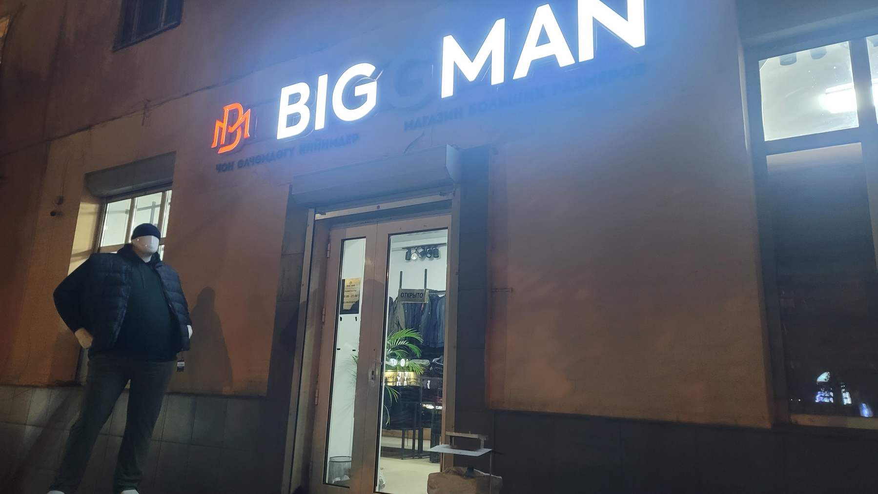 BIGGMAN letters lit above a shop entrance, except for the second G, so the shop name reads like Big Man. Mannequin with a belly dressed in men's clothes by the door