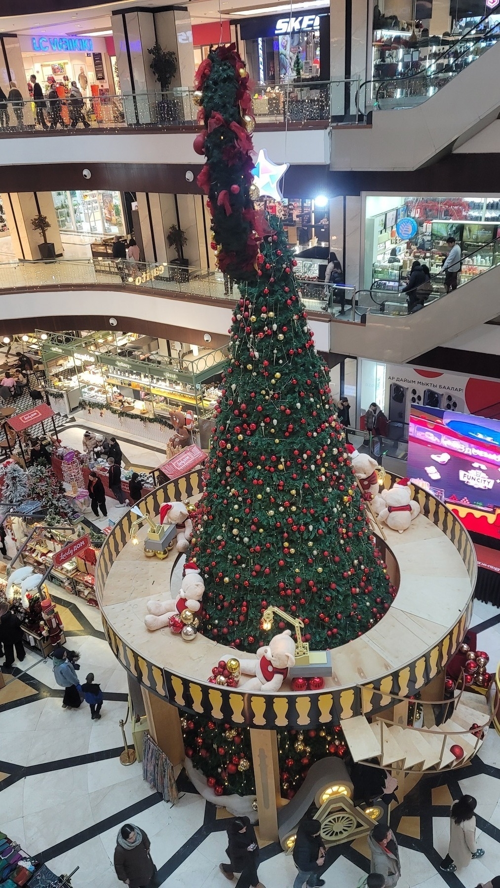 two floor high Christmas tree in the center of the ground floor of a mall