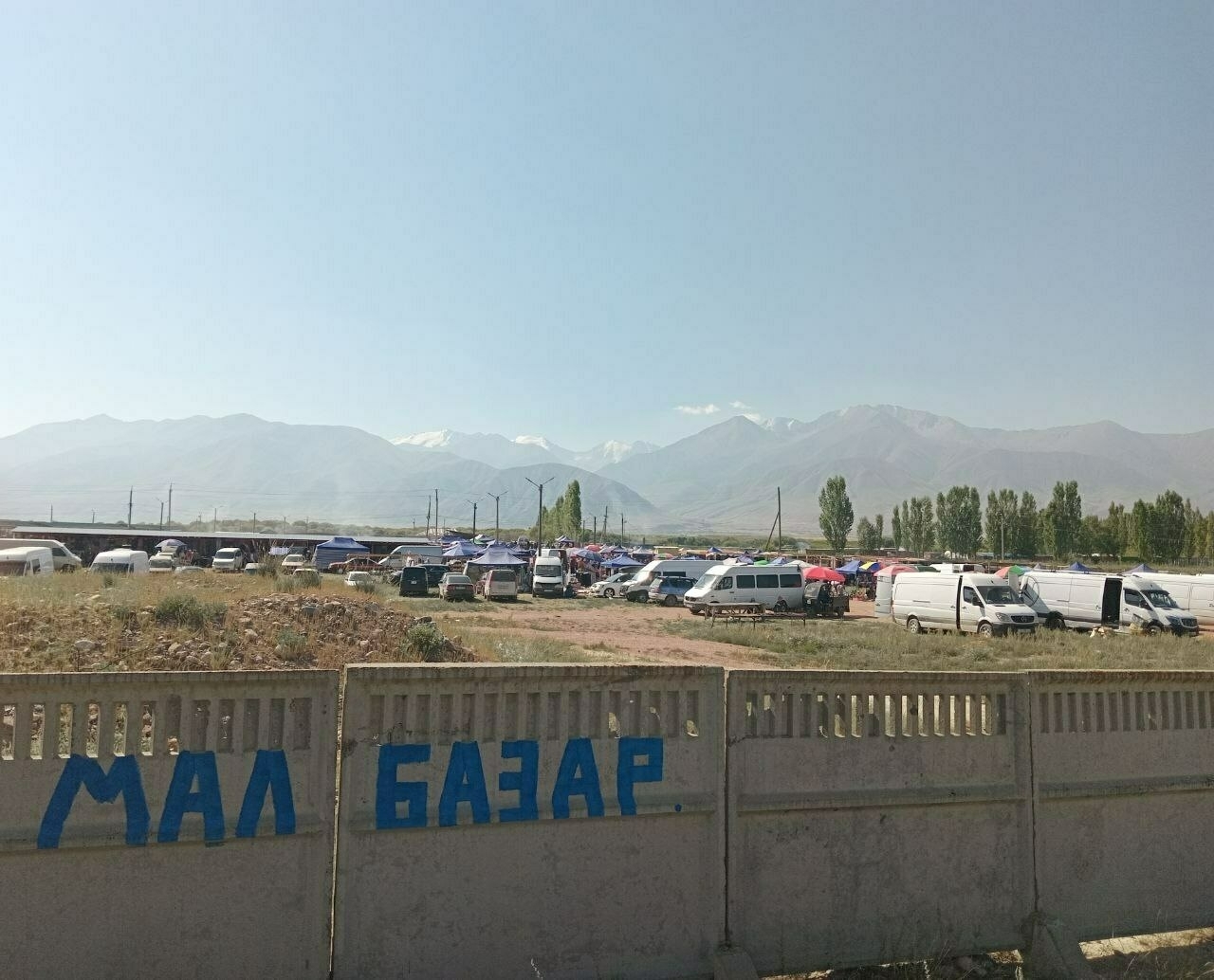 A lot of vans and cars parked in the distance behind a concrete fence. Mountains even further in the distance