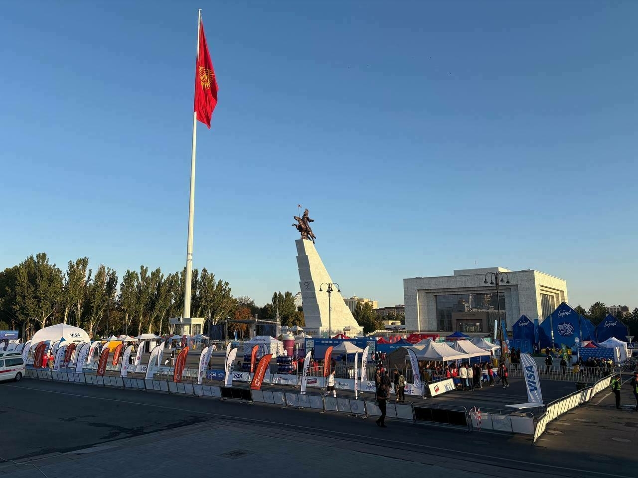tents and fences set up at Ala-Too Square with a sculpture and the Kyrgyz flag in the background