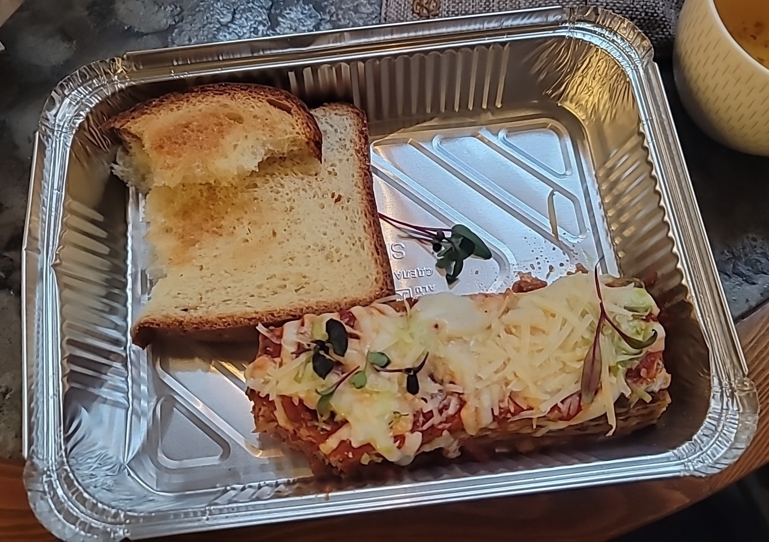 Bread and piece of lasagna with one small bite taken out of it in a foil to-go container