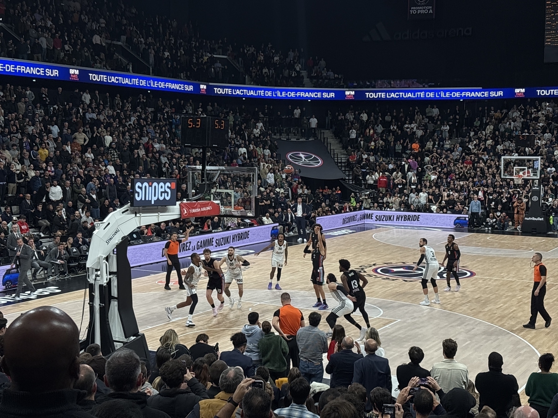 A basketball game is taking place in a crowded arena, with players on the court and spectators watching.