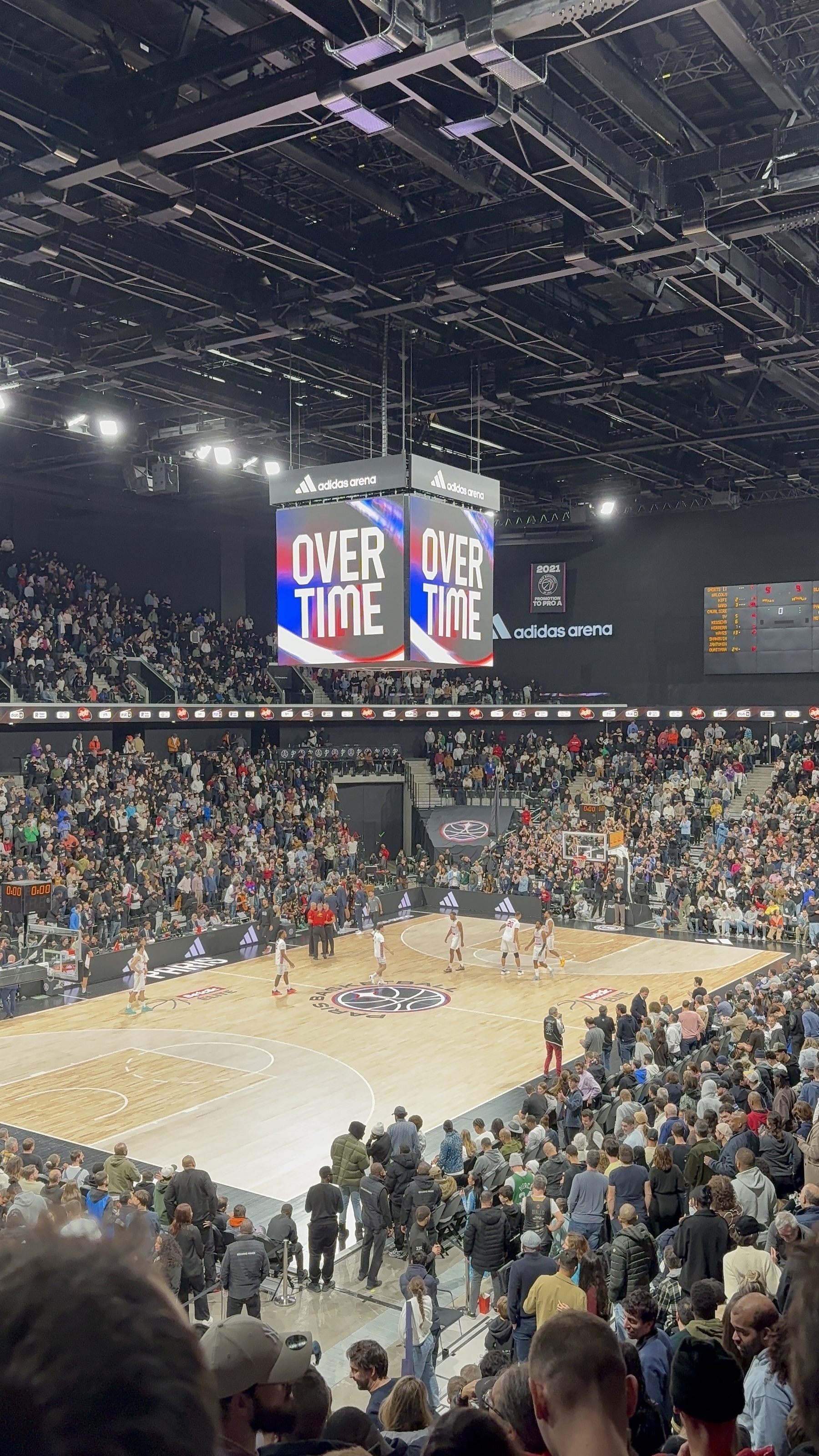 A basketball game is taking place in an arena filled with spectators, with the scoreboard showing "Overtime."