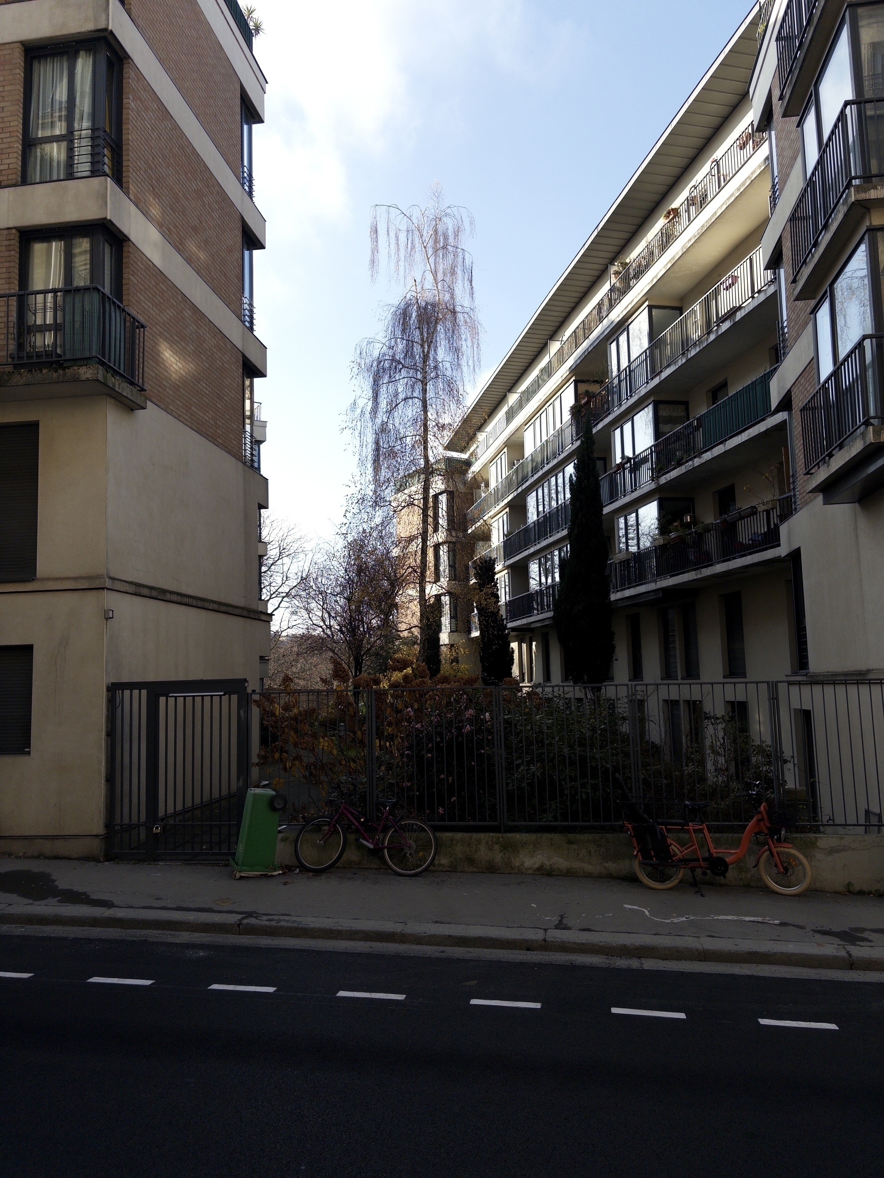 A street with buildings on either side, containing a few parked bicycles and trees, under a clear sky.