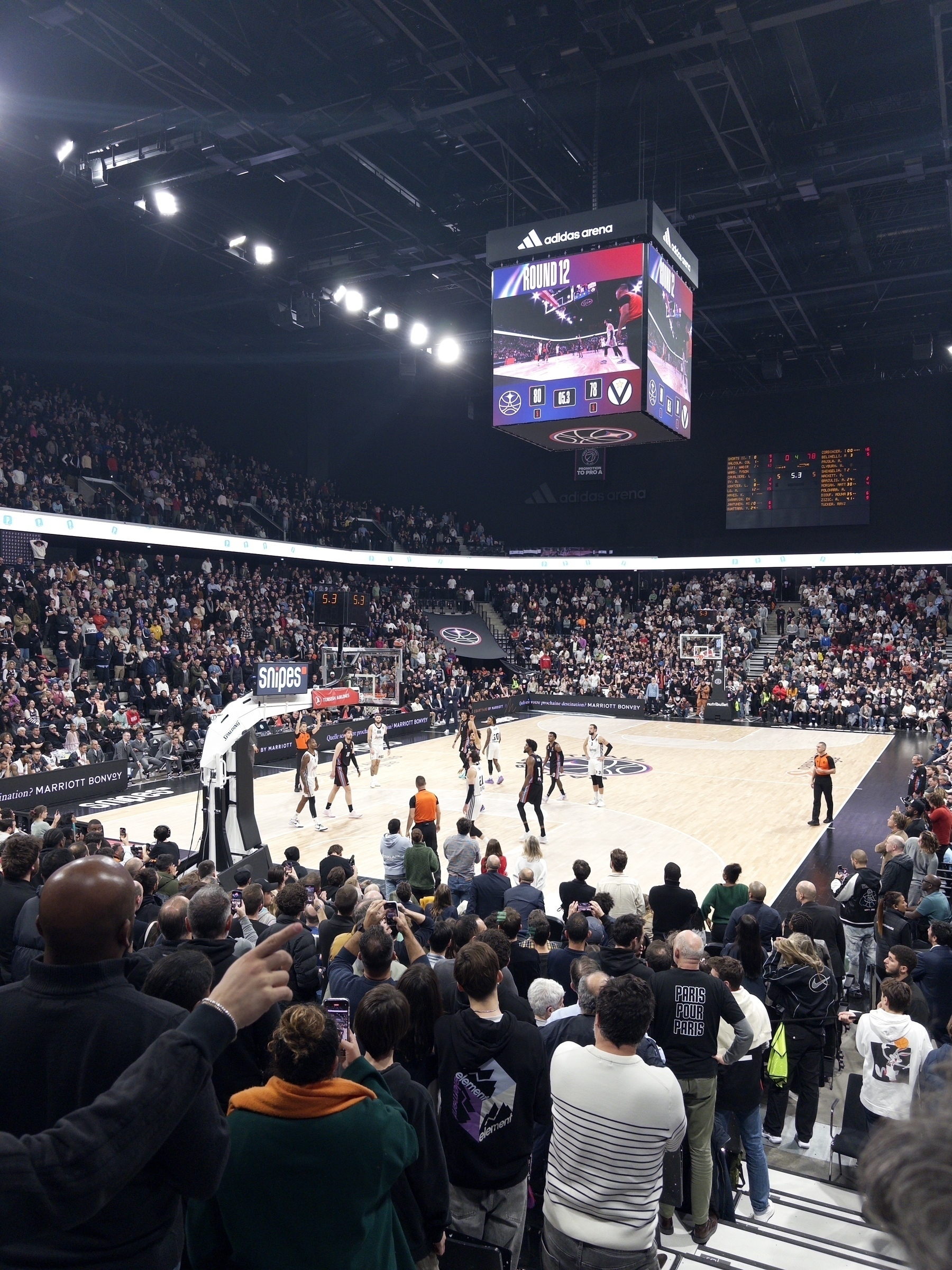 A crowded basketball arena is filled with spectators watching an ongoing game.