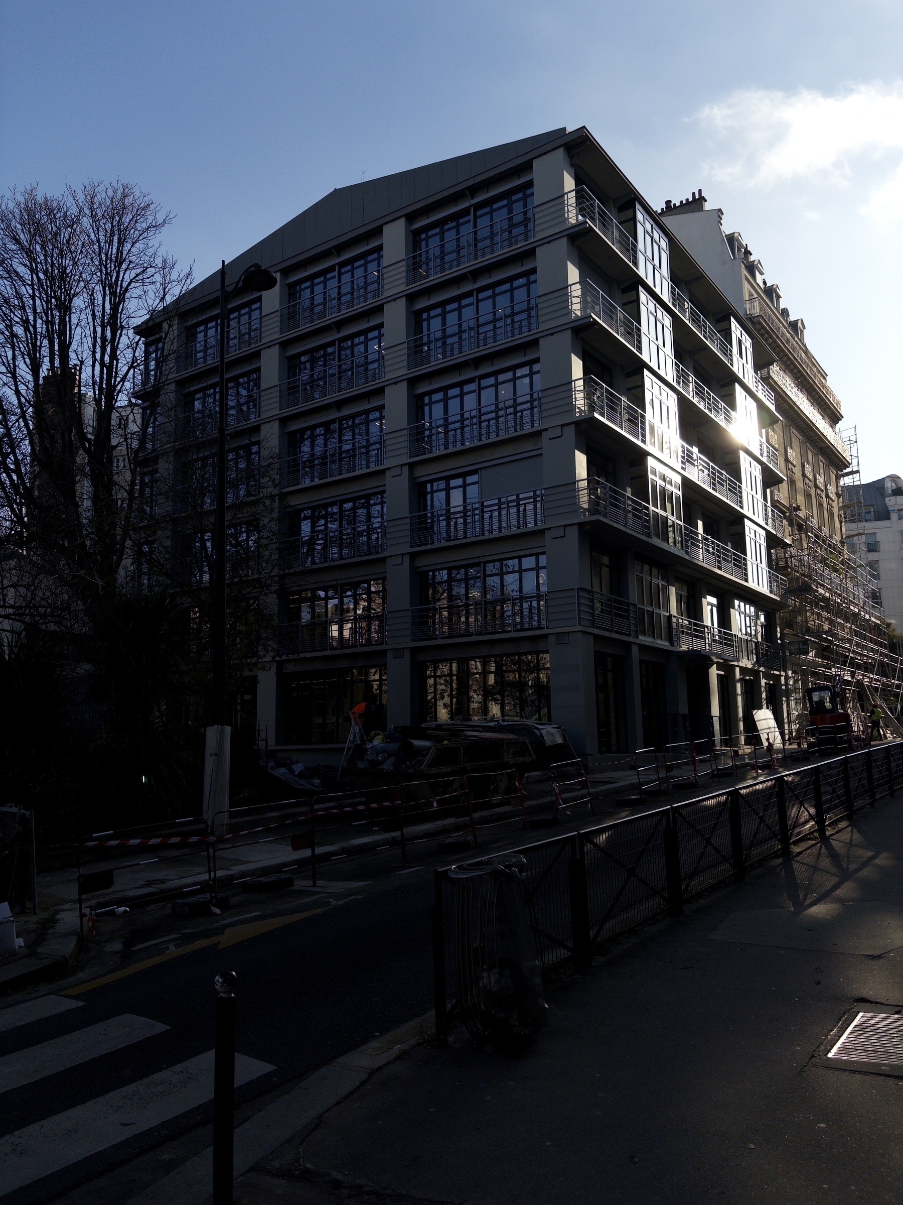 A modern, multi-story office building is under construction or renovation, with scaffolding and a quiet street in the foreground.