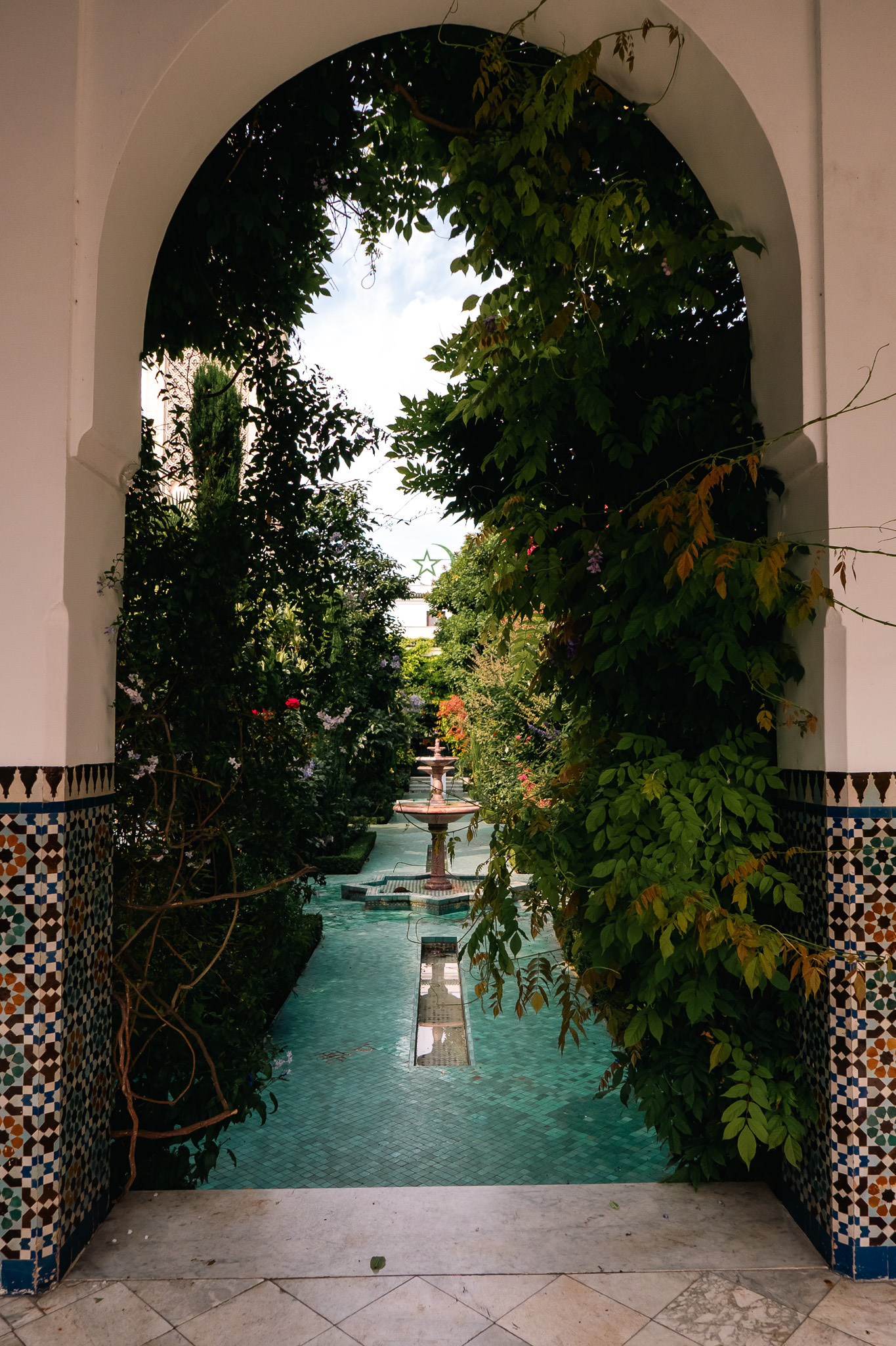 A lush garden with a central fountain is framed by an ornate archway and vibrant greenery.