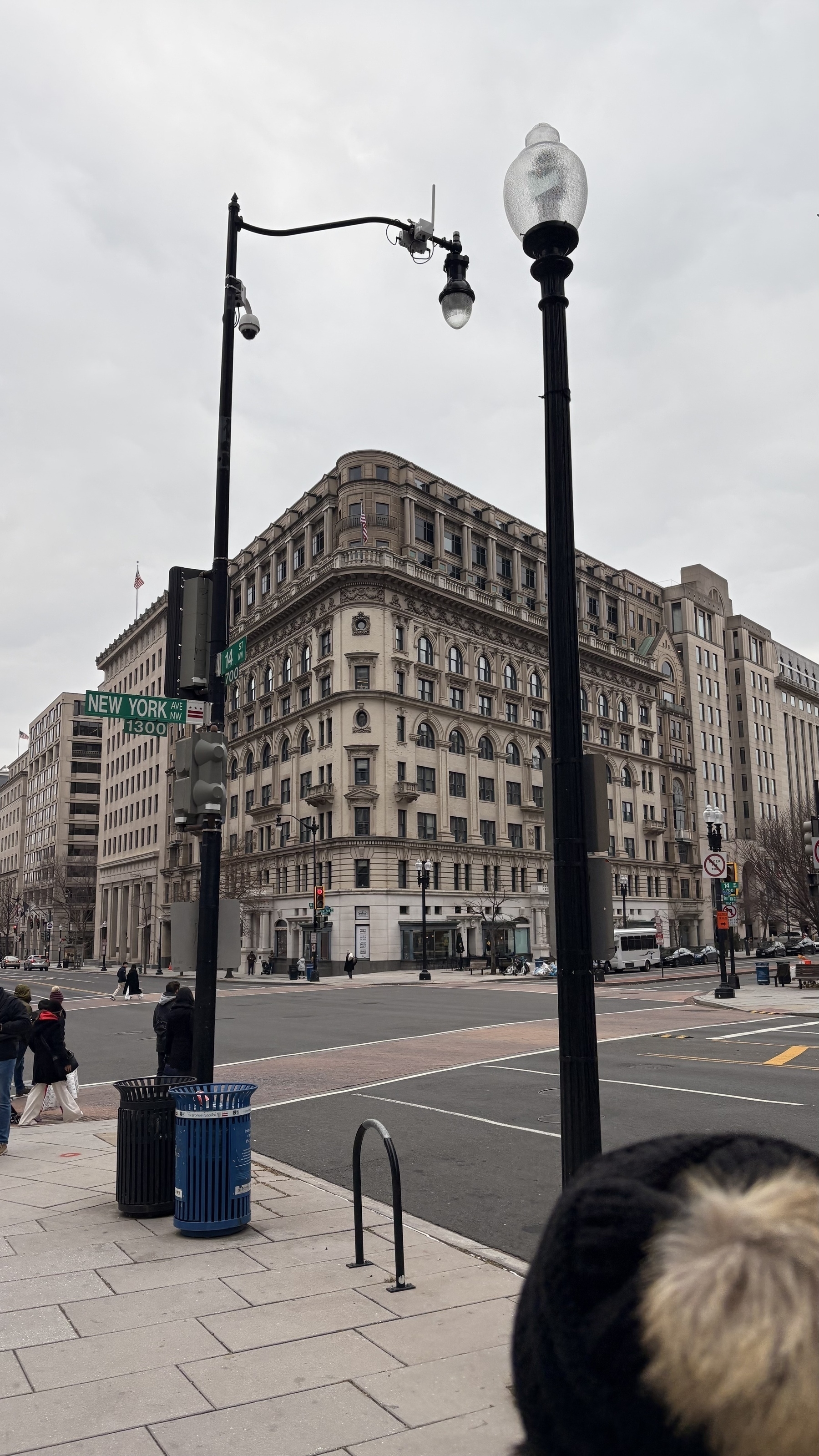 A historic multi-story building stands at a street corner with a street sign and lampposts under a cloudy sky.