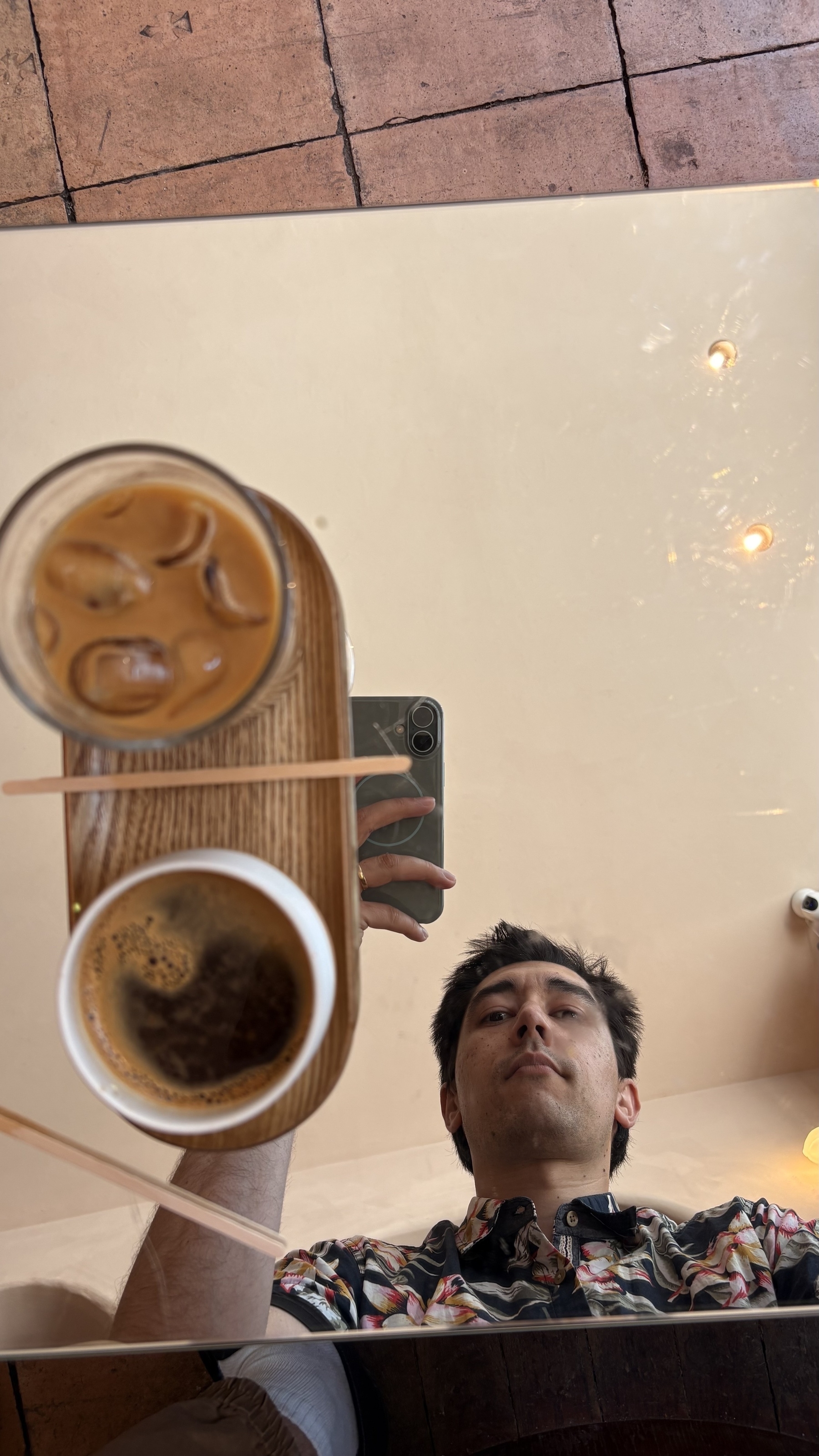 A person is taking a photo of their reflection in a mirrored table with two cups of coffee on it.