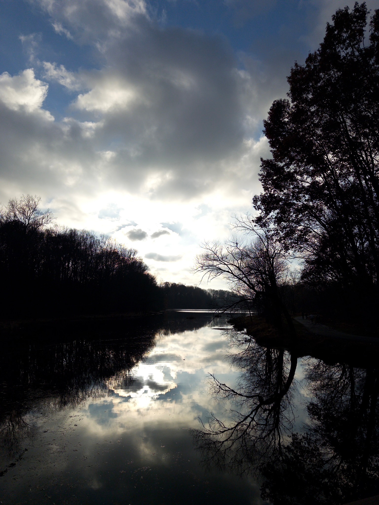 A tranquil river reflects the dramatic sky and silhouetted trees at dusk.