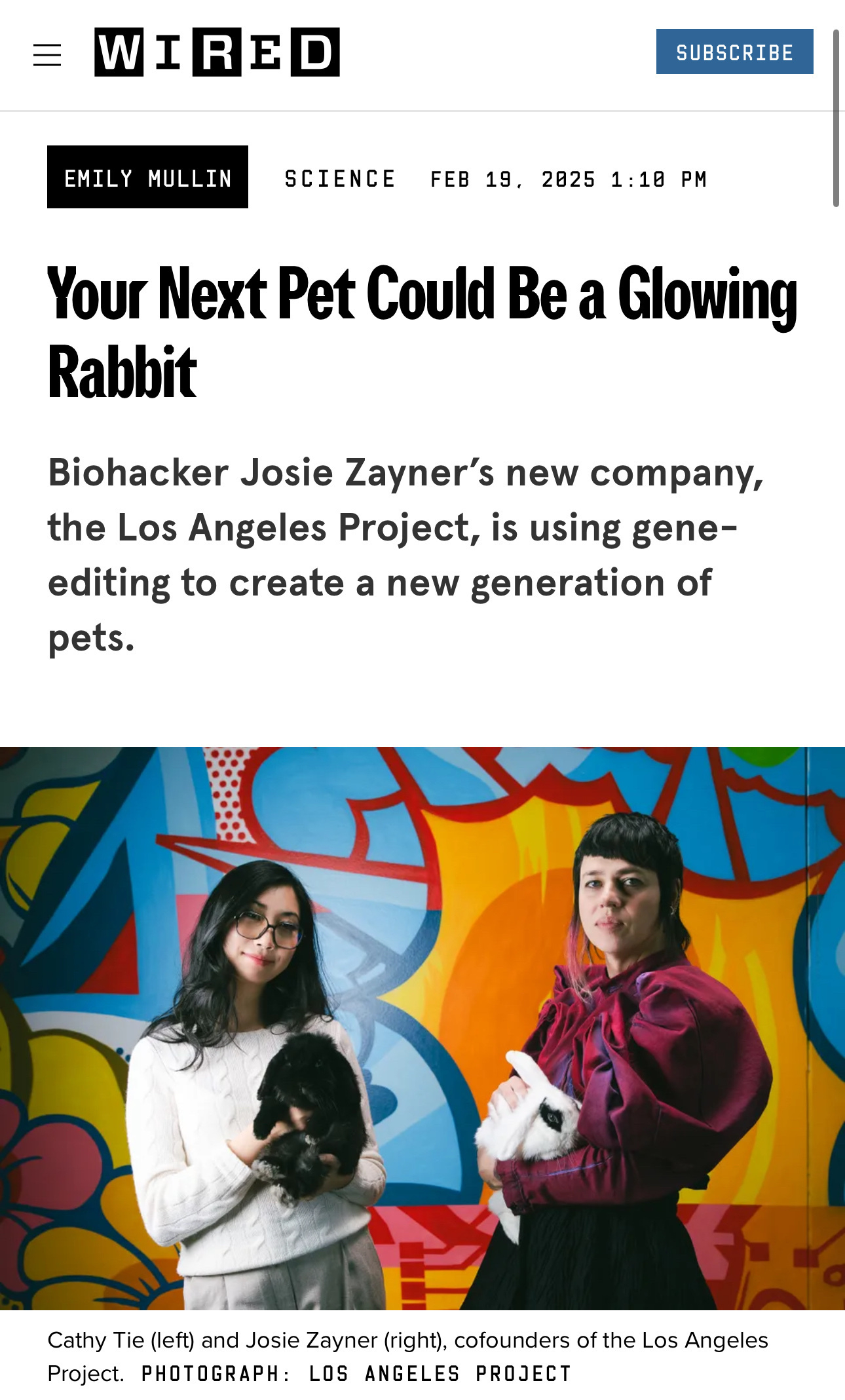 Two women pose in front of a colorful mural, associated with a Wired article about biohacking and genetically engineered glowing rabbits.