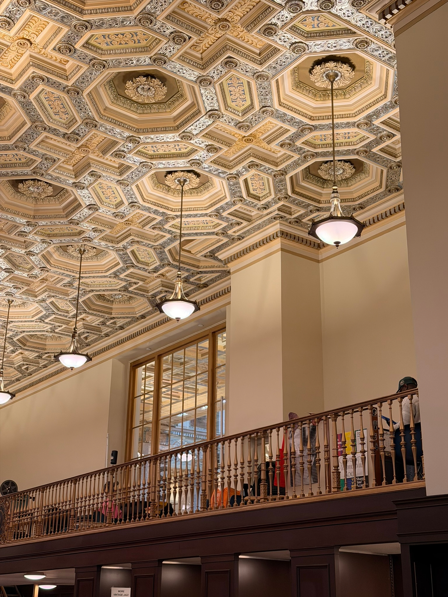 A grand interior features an ornate hexagonal coffered ceiling, elegant light fixtures, and a wooden balcony railing.