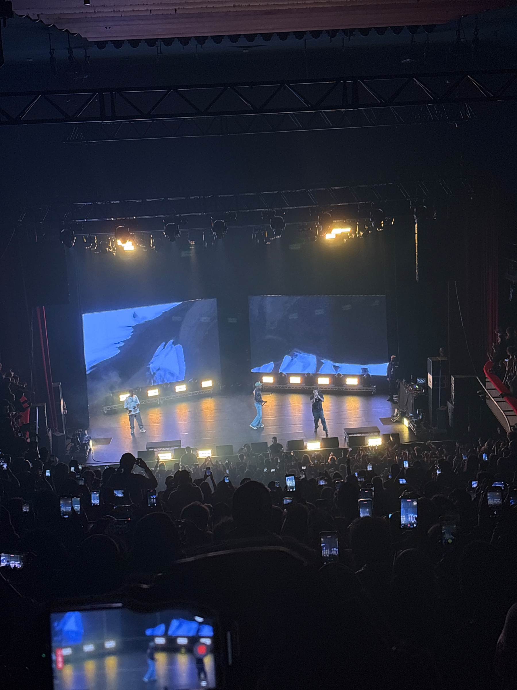 A concert stage features performers under bright lights, with the word CLIPSE displayed on large screens and a crowd watching.