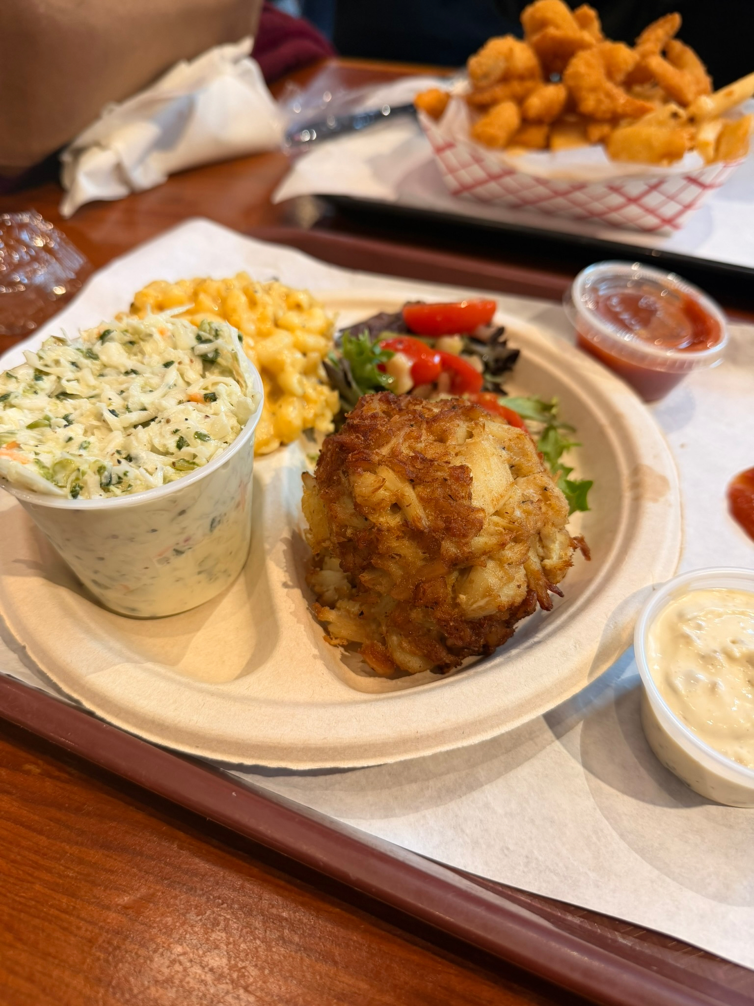A plate featuring a crab cake, macaroni and cheese, and a container of spinach dip is served alongside a side of fried shrimp.
