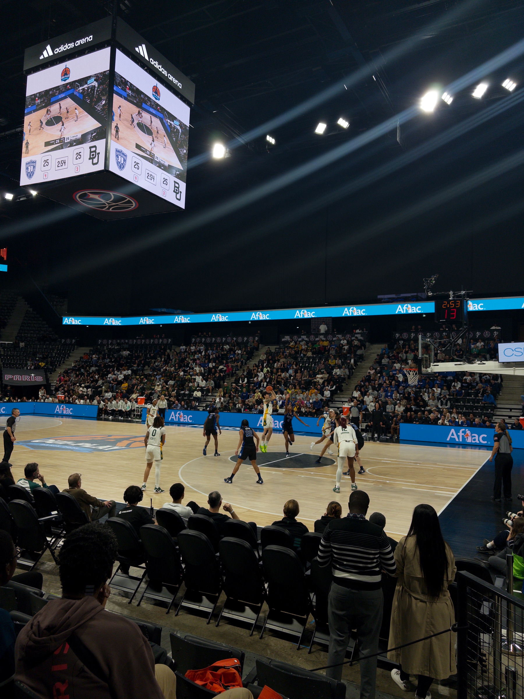 A basketball game is taking place in an indoor stadium with players on the court and spectators watching.