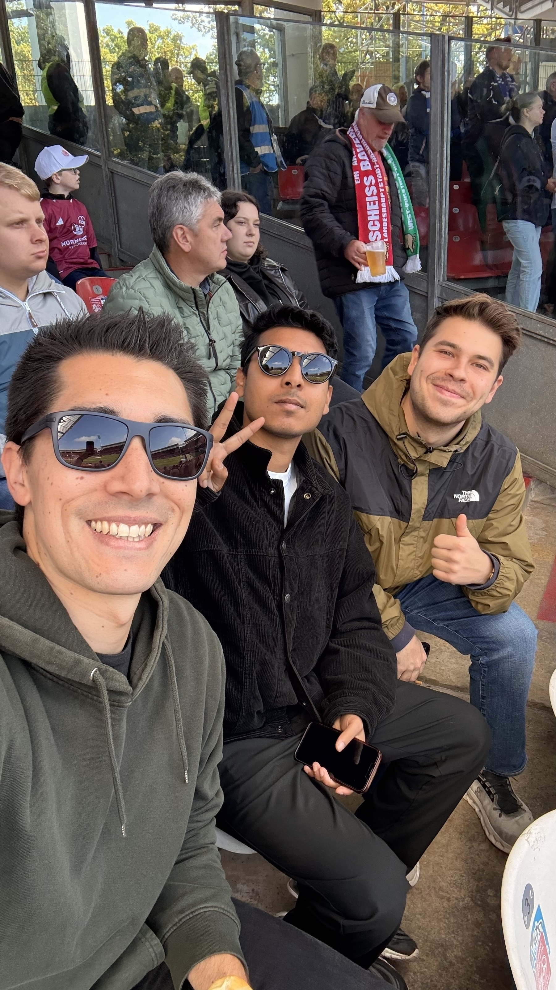 Three friends are sitting in a stadium, smiling and posing for a selfie.
