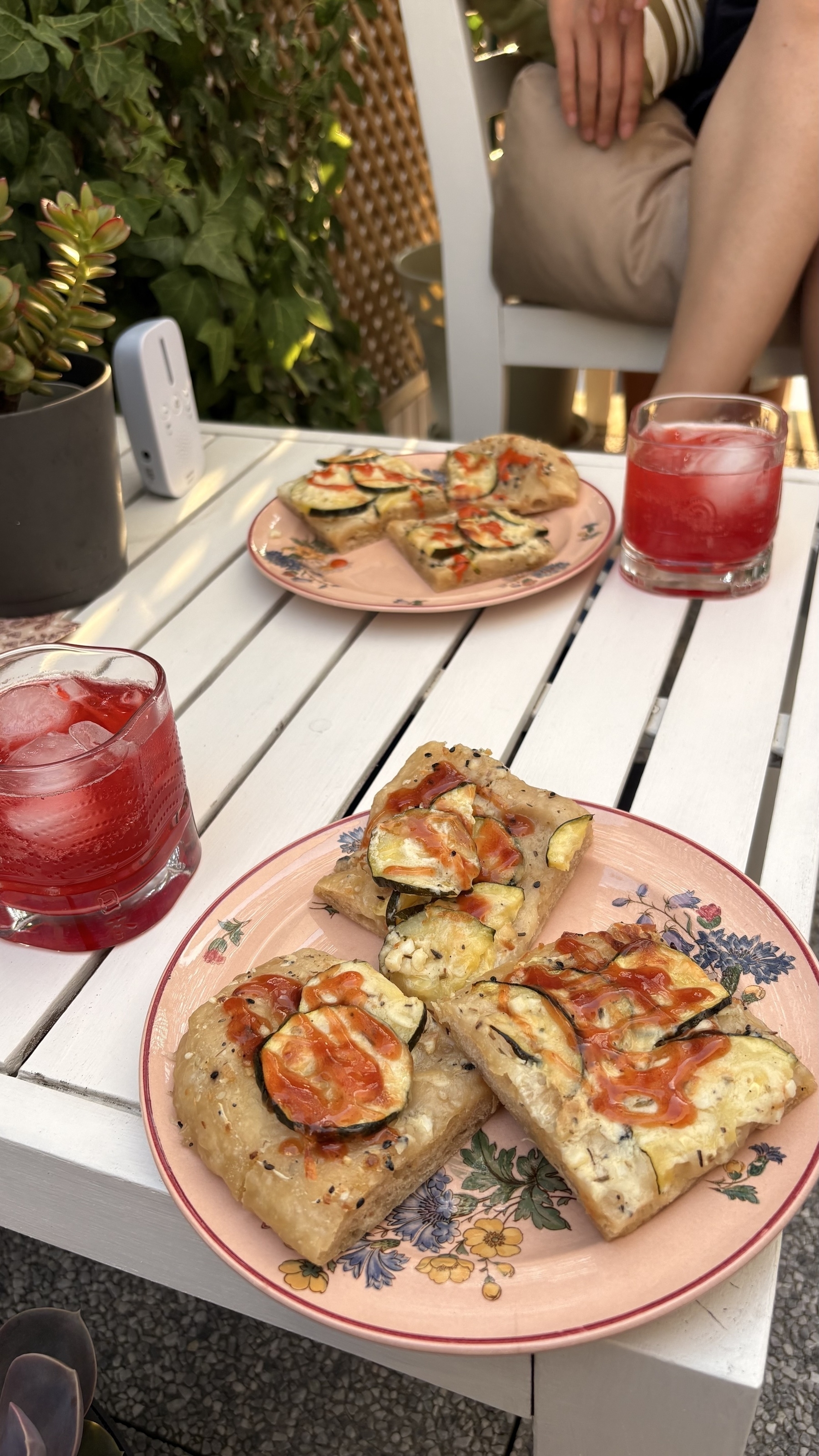 Appetizing flatbreads topped with vegetables are served on a table alongside two red drinks.