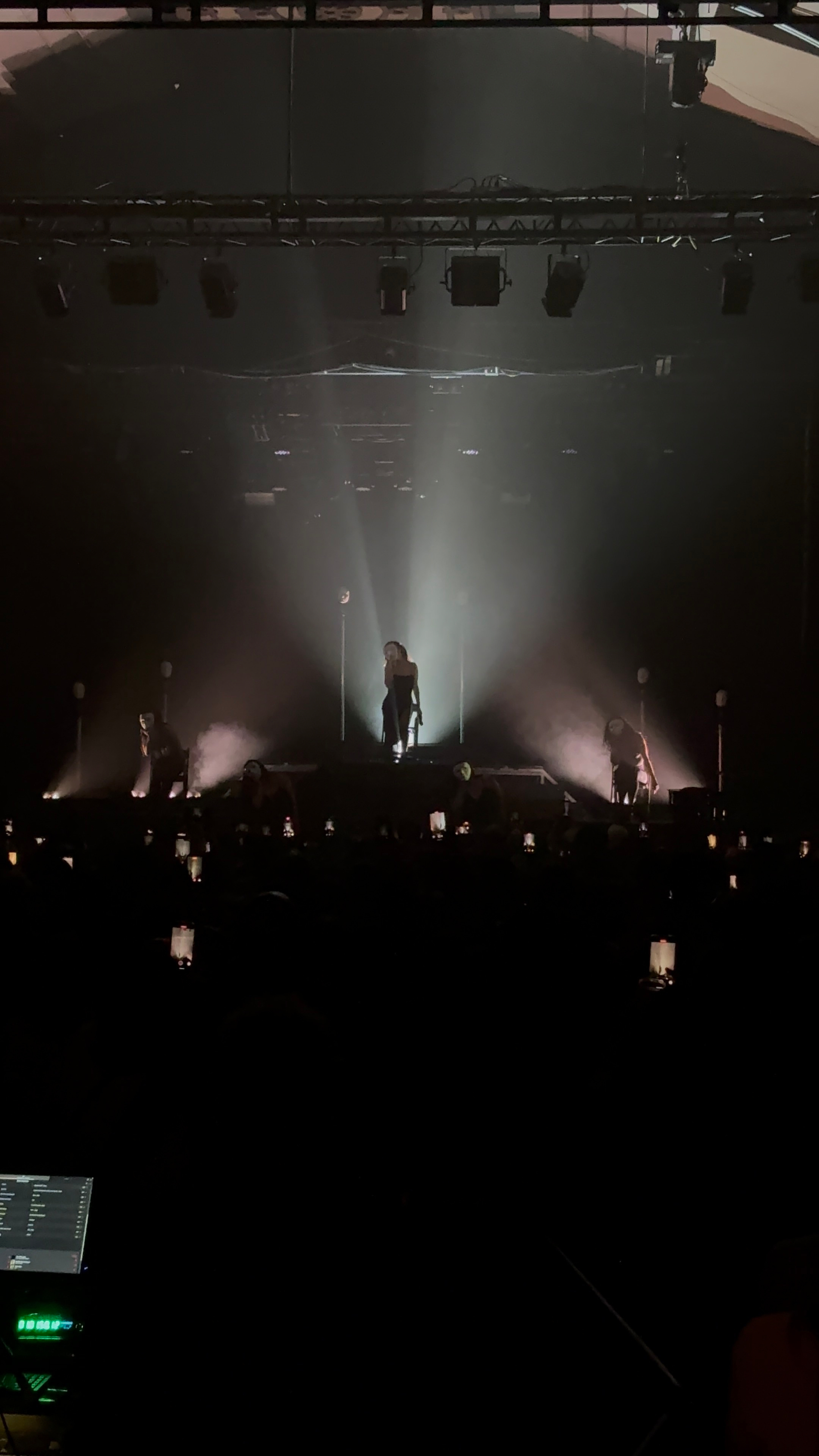 A performer stands dramatically on stage with backlighting, surrounded by musicians in a dark concert setting.