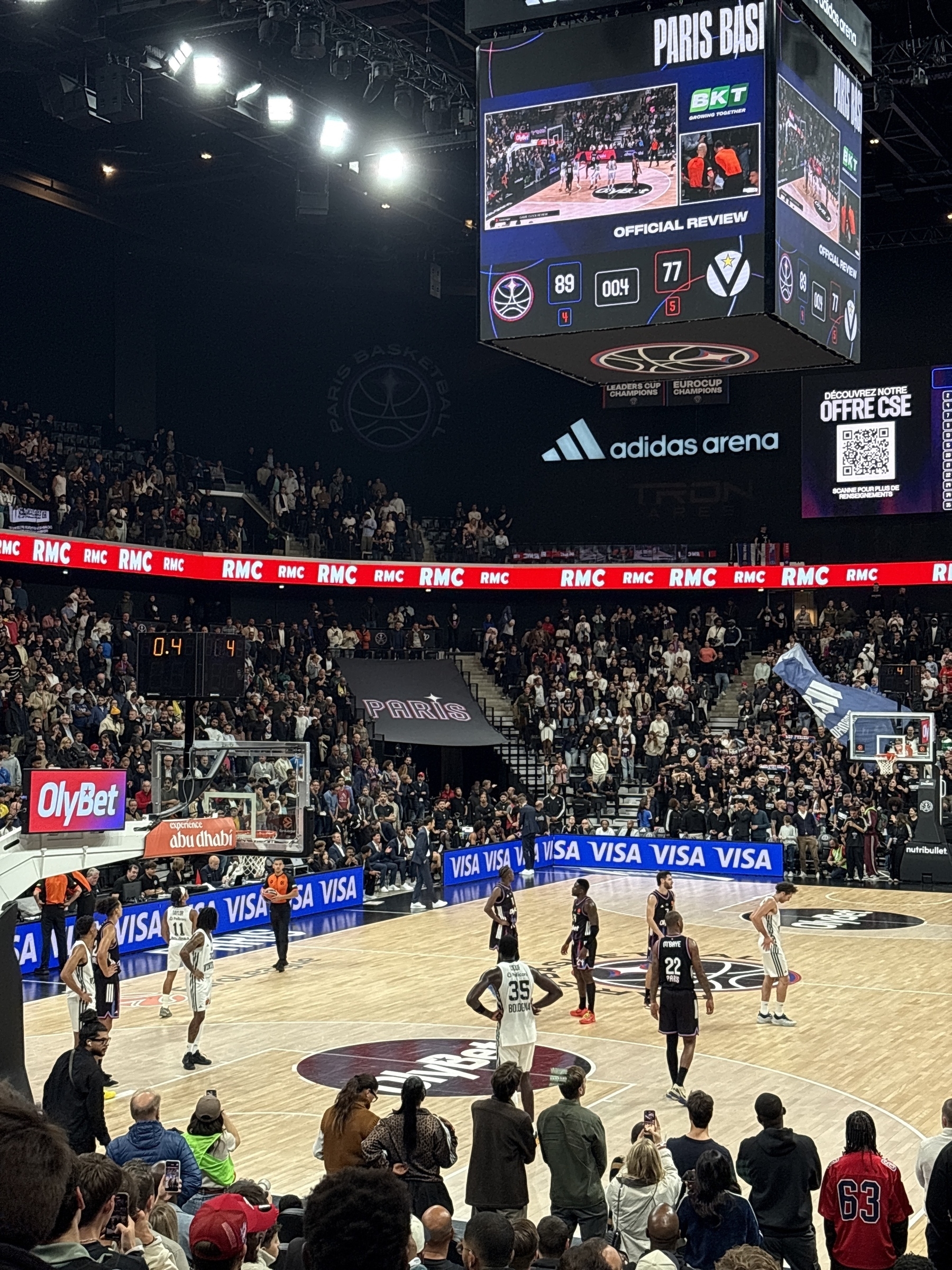 A basketball game is underway in a lively arena, featuring a match between two teams with a score of 89-77 displayed on the scoreboard.