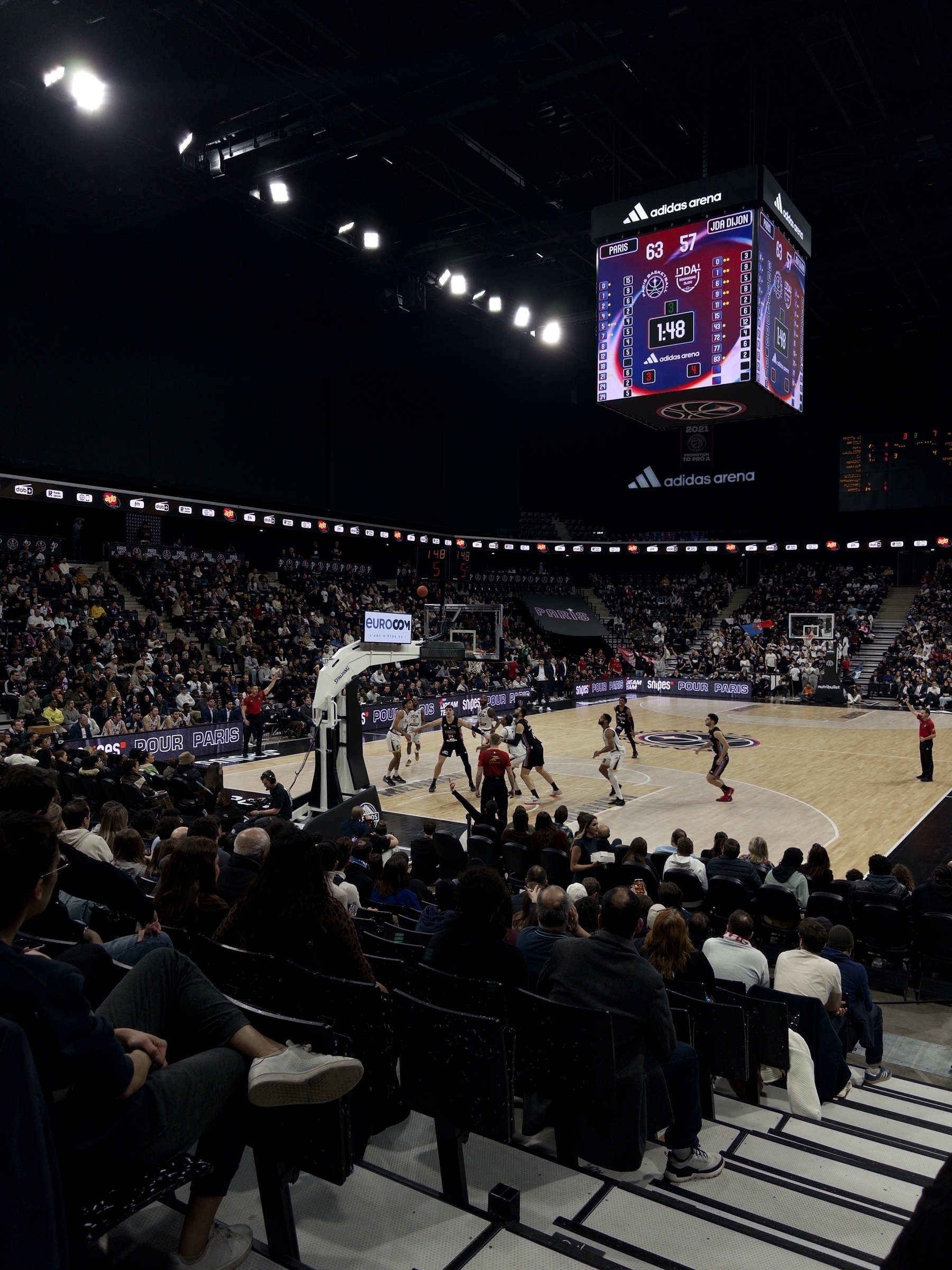 A basketball game is being played in a large indoor arena with a scoreboard displaying the score and time.