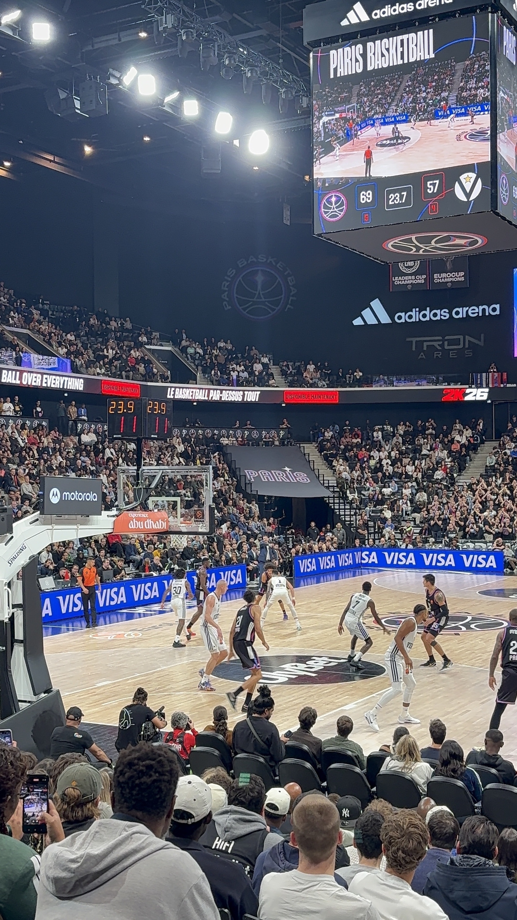 A basketball game is in progress at a crowded arena, with players actively engaged on the court and fans watching.