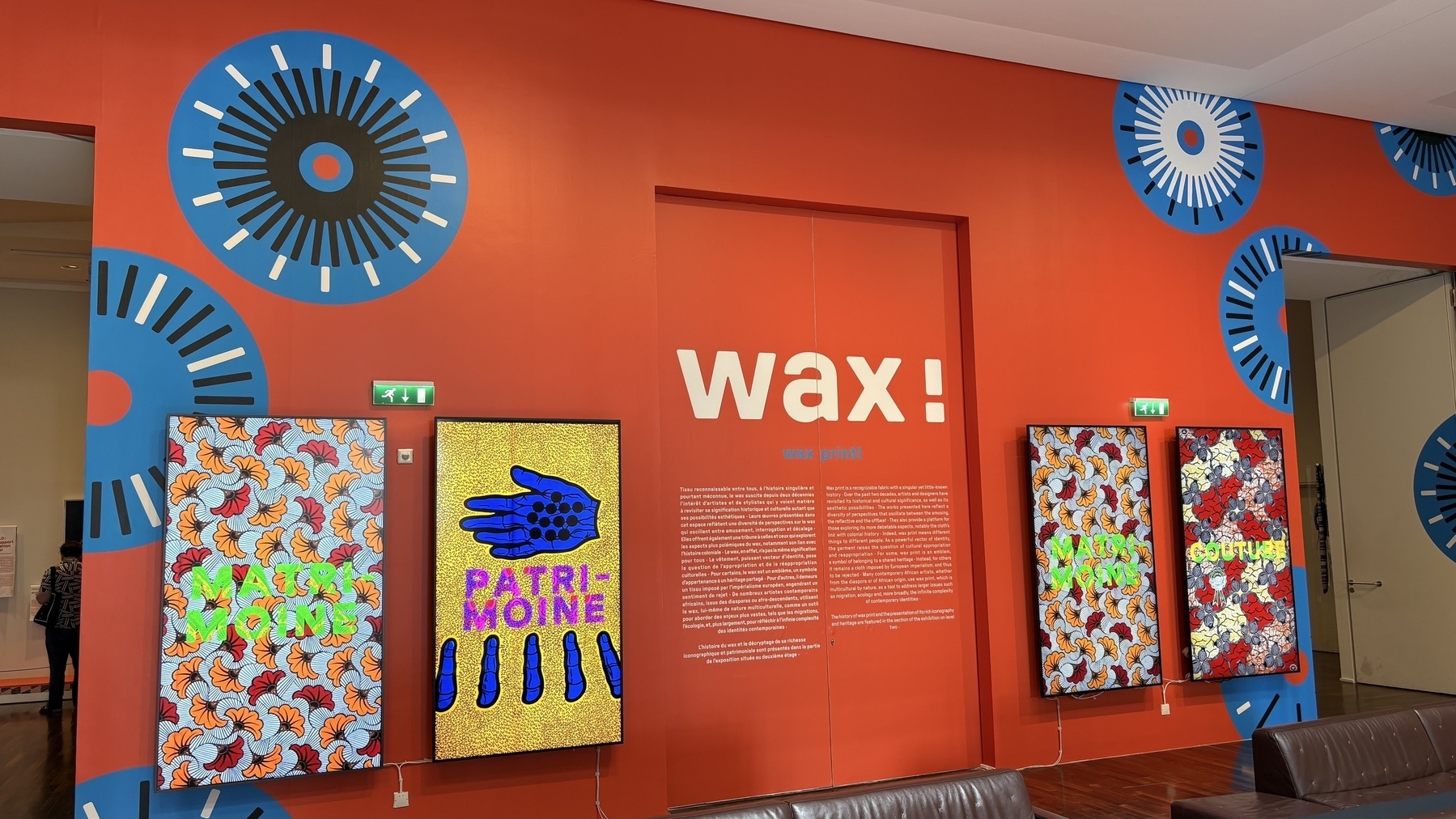 A vibrant red wall features digital displays with various colorful patterns and the bold word "wax" in the center.