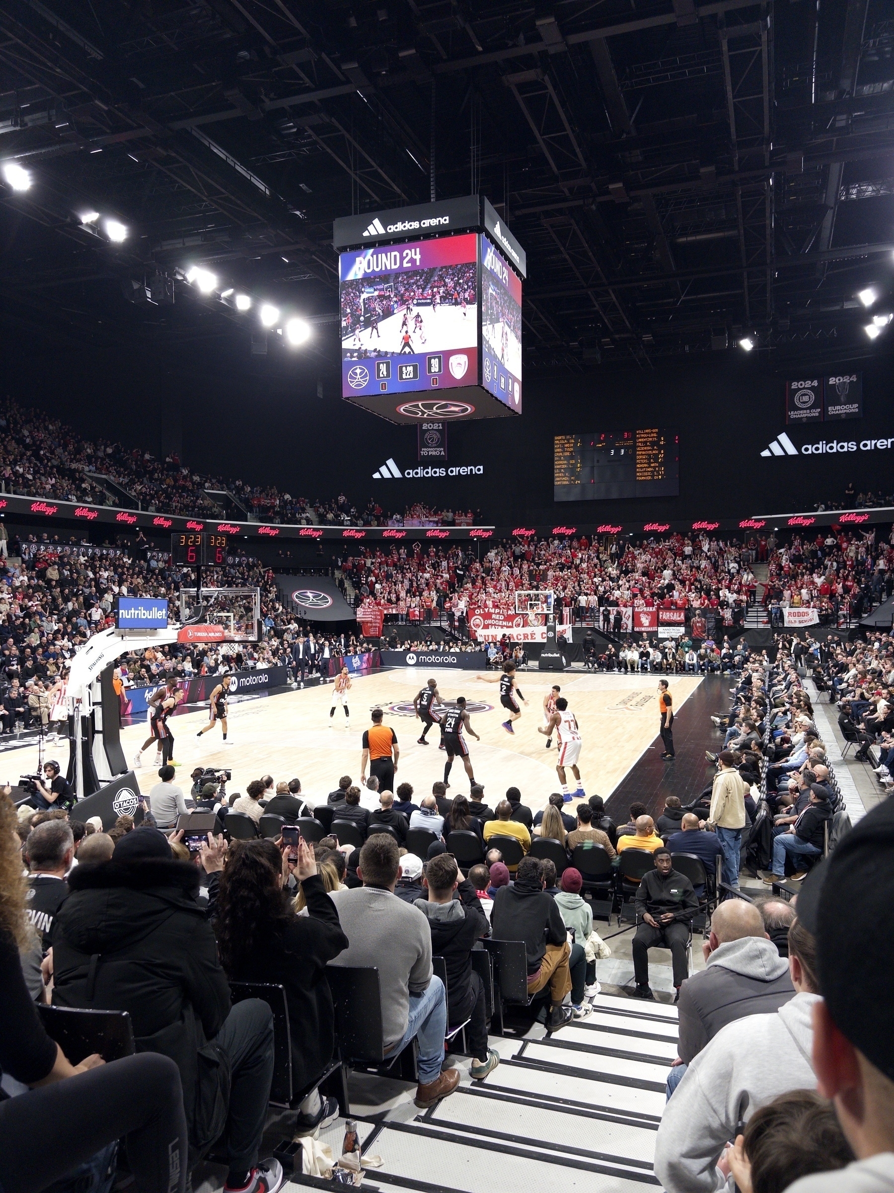 A basketball game is taking place in a crowded indoor arena with spectators watching intently.