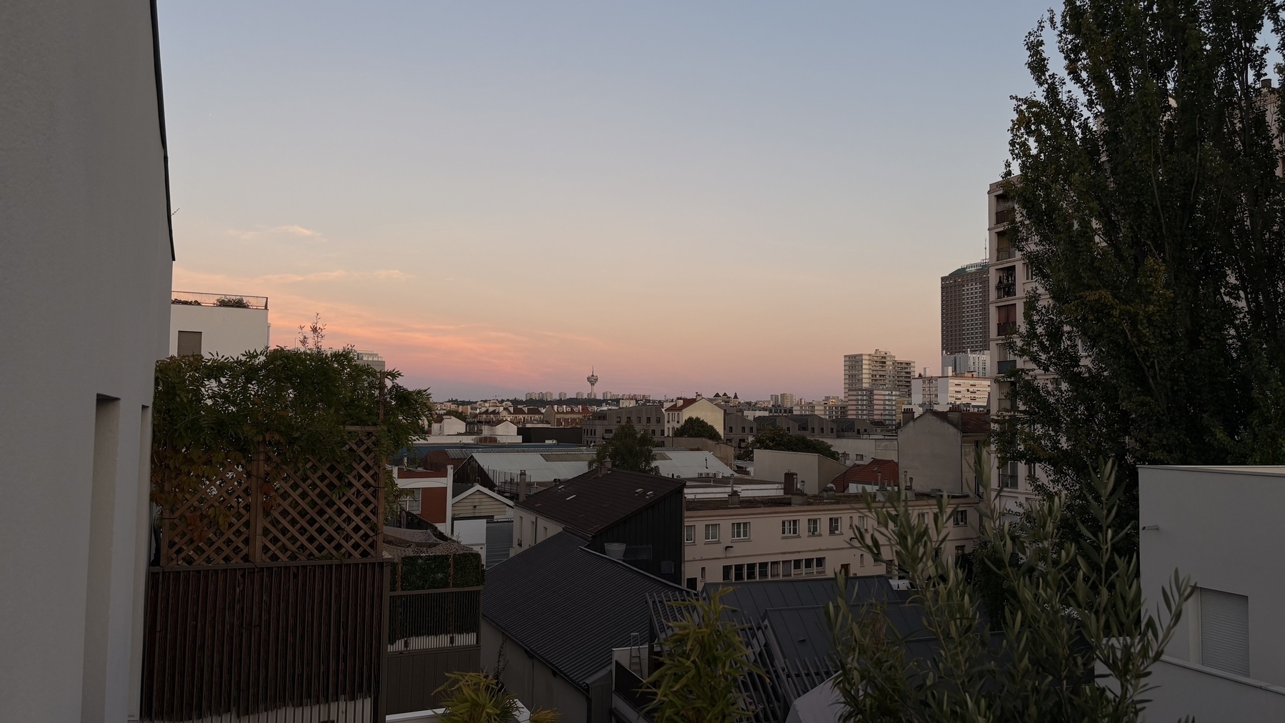 Urban landscape at sunset with buildings and trees against a colorful sky.