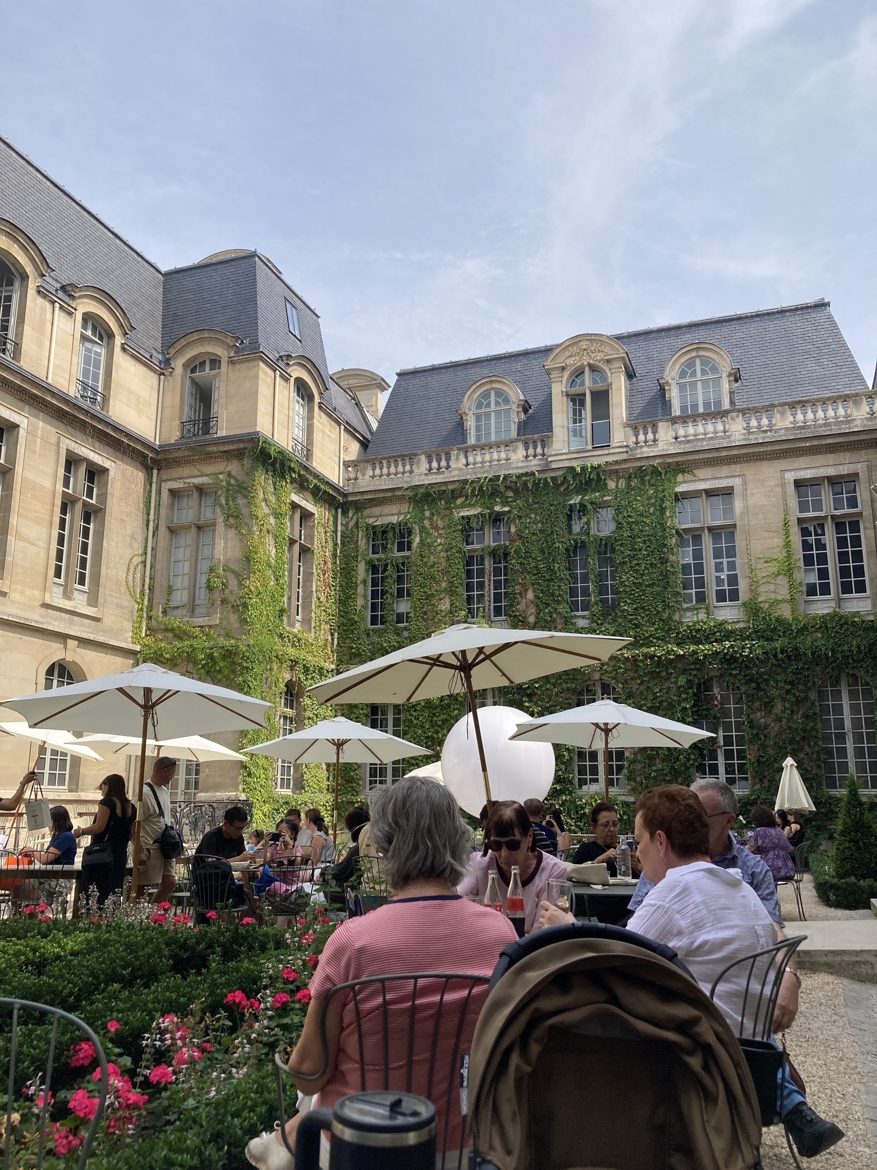 People are dining outdoors in a courtyard with historic architecture and ivy-covered walls.