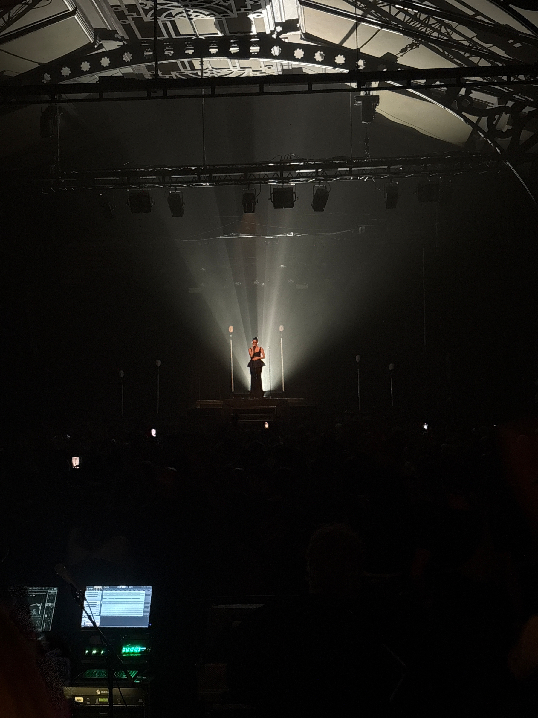A performer stands on a dimly lit stage with dramatic spotlights creating a striking effect.