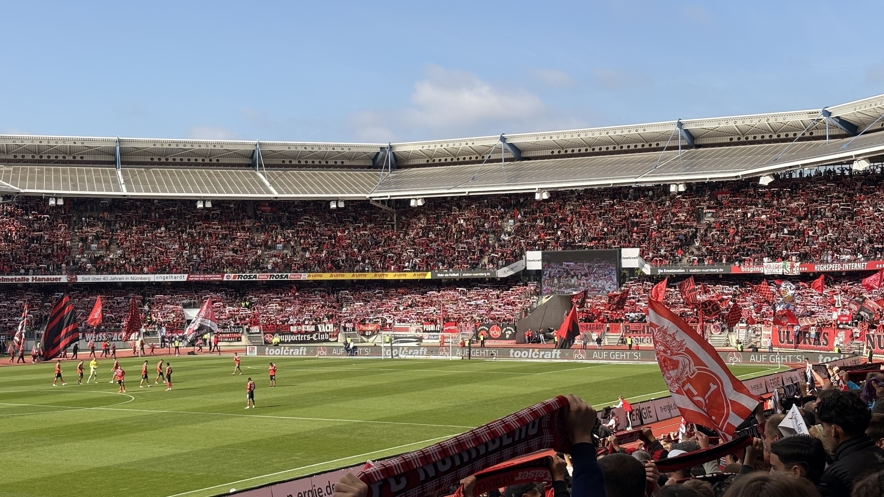 A crowded soccer stadium is filled with fans waving red and white flags and banners while players are on the field.