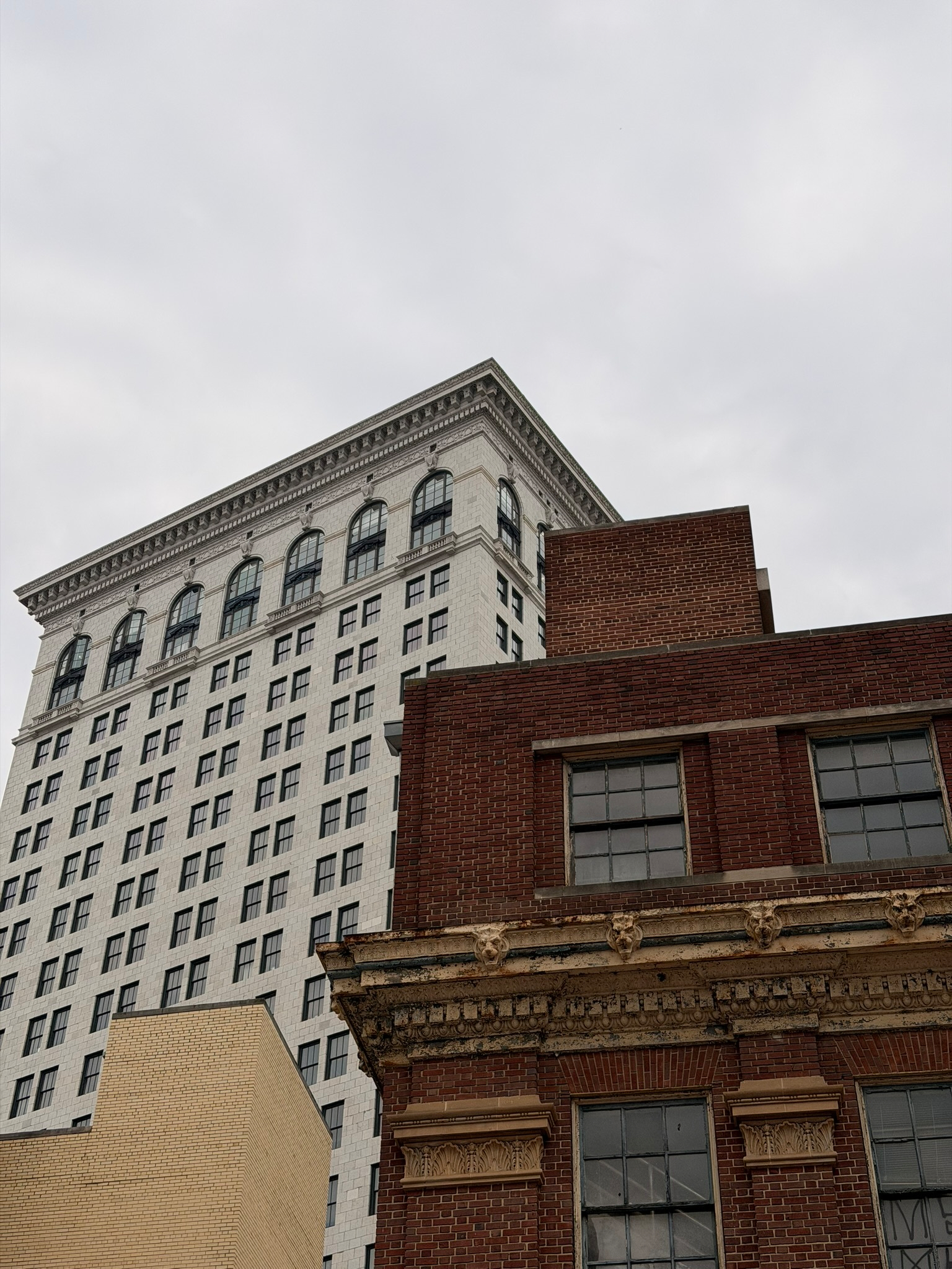 A contrast of architectural styles is depicted with a modern white building and an older brick structure against a cloudy sky.