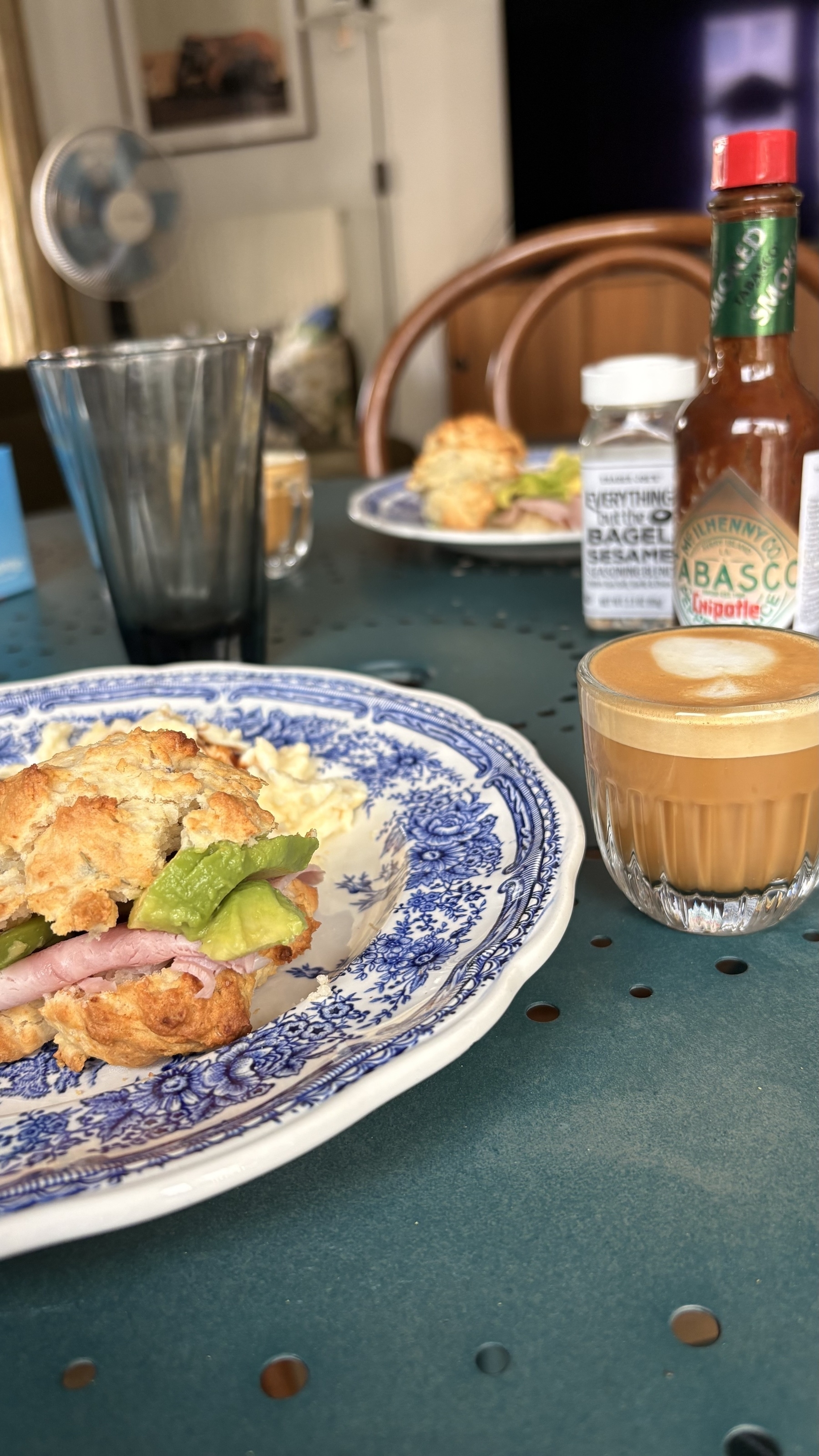 A breakfast setup with a plate of food and a glass of coffee on a table, featuring items like Tabasco sauce and seasoning.