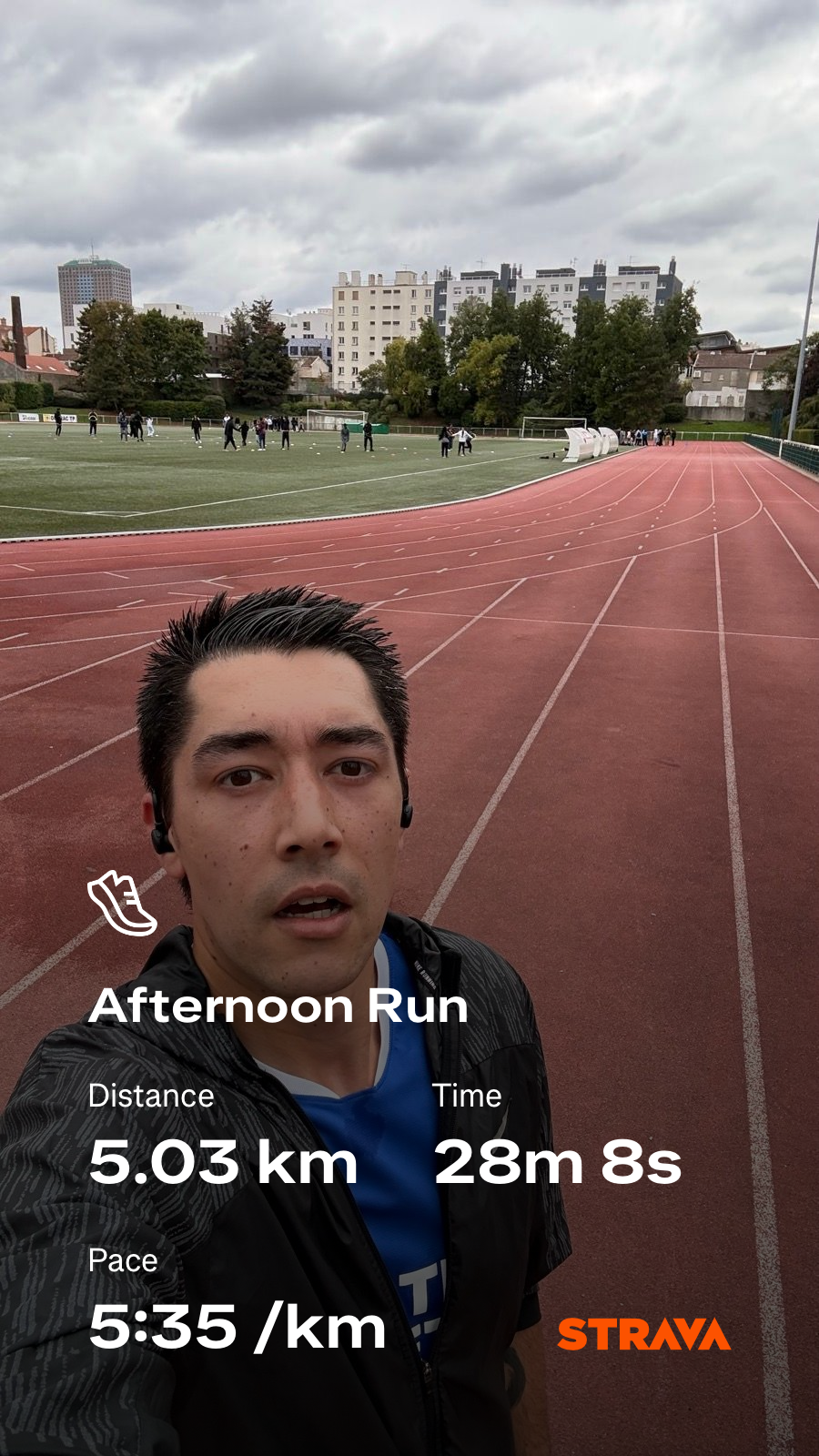 A man is on a running track with an overlay showing the details of his afternoon run, including distance, time, and pace using the Strava app.