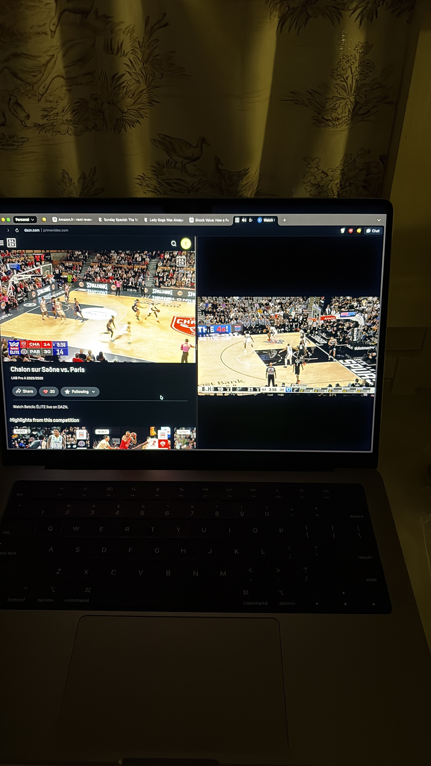 A laptop screen displays two split basketball game livestreams in a dimly lit room.