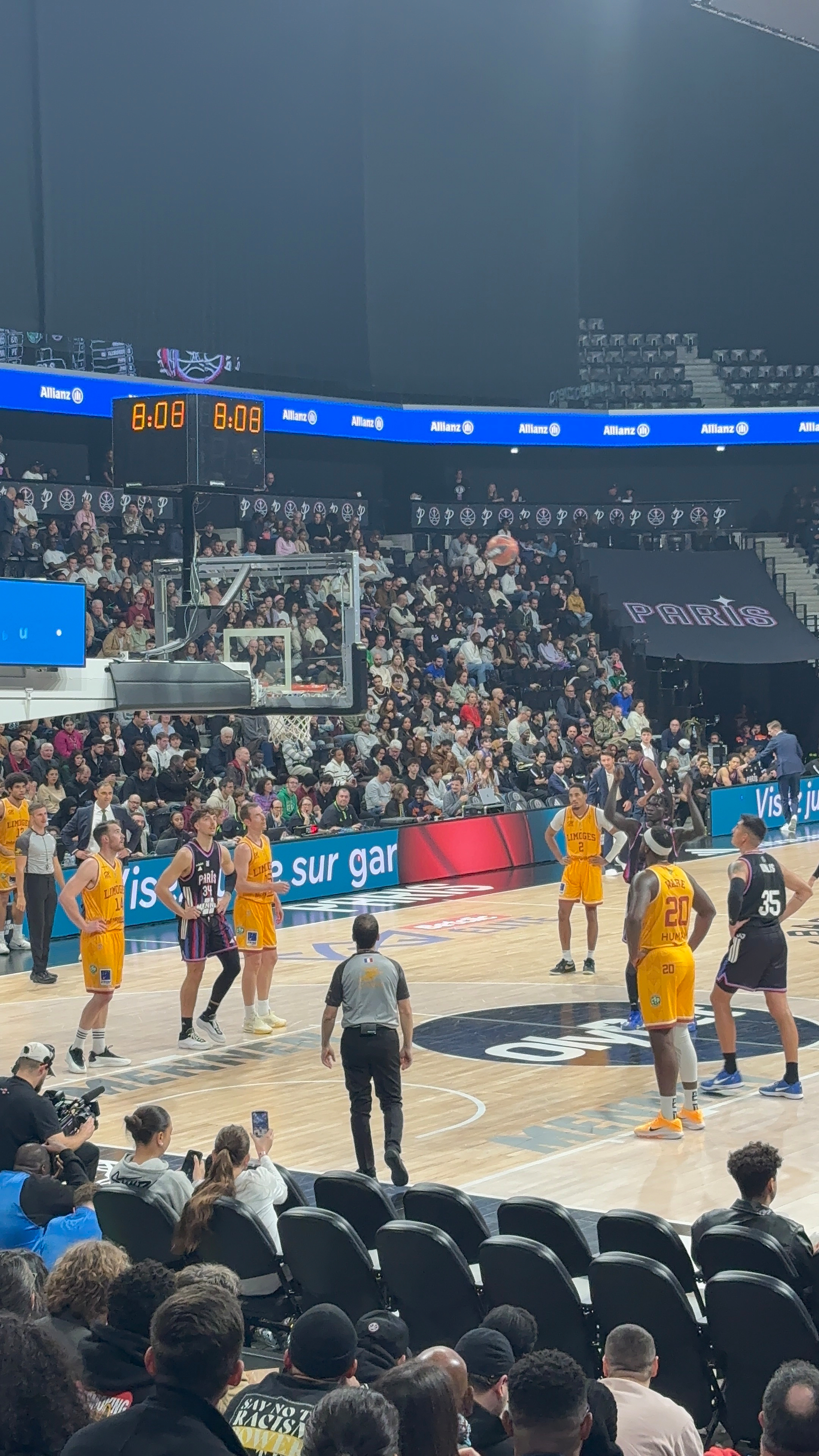 A basketball game is taking place with players from opposing teams positioned for a free throw in front of a large audience.