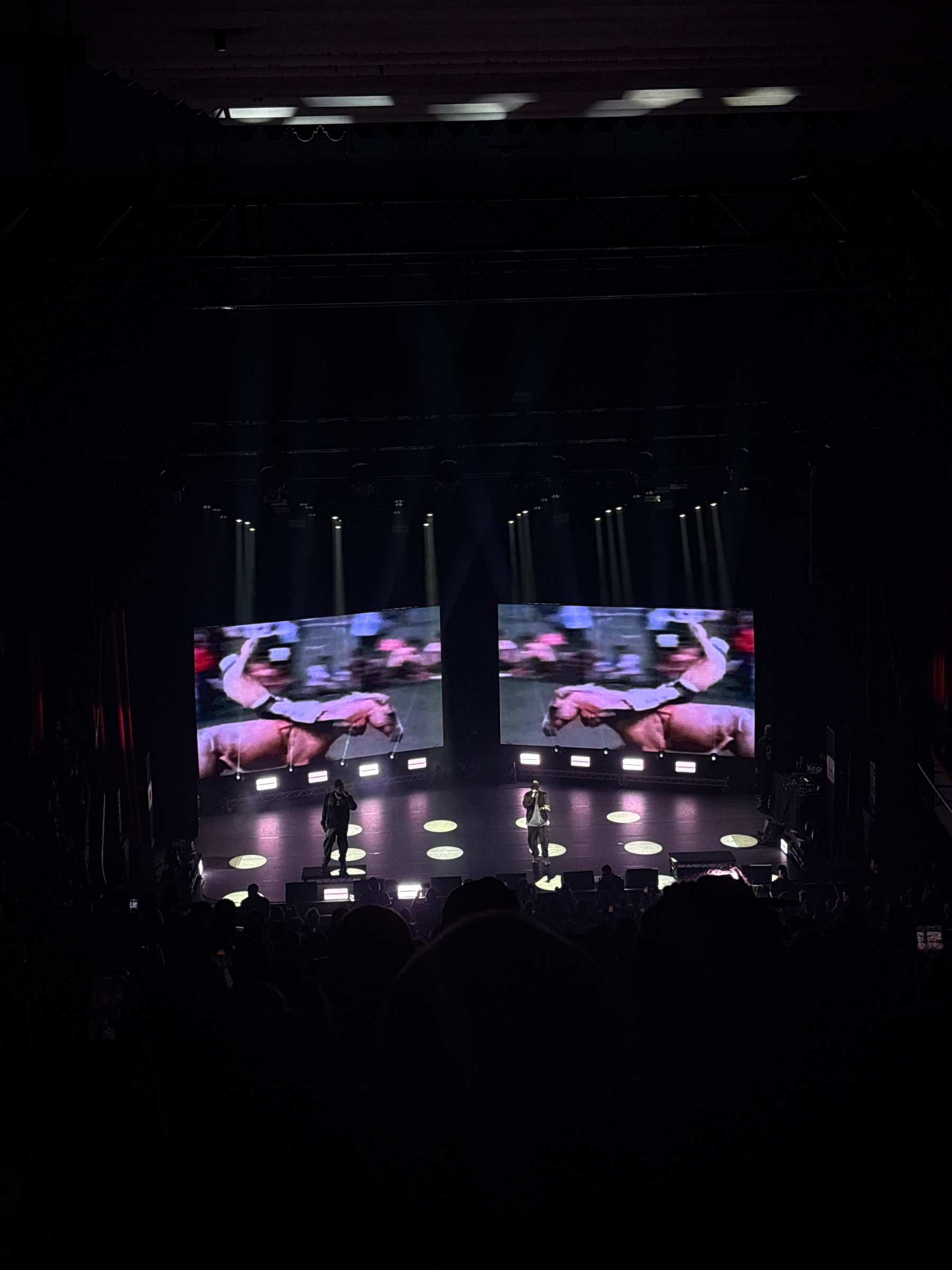 A concert scene features a lit stage with performers, a large screen displaying a performer, and an audience in a dimly lit venue.
