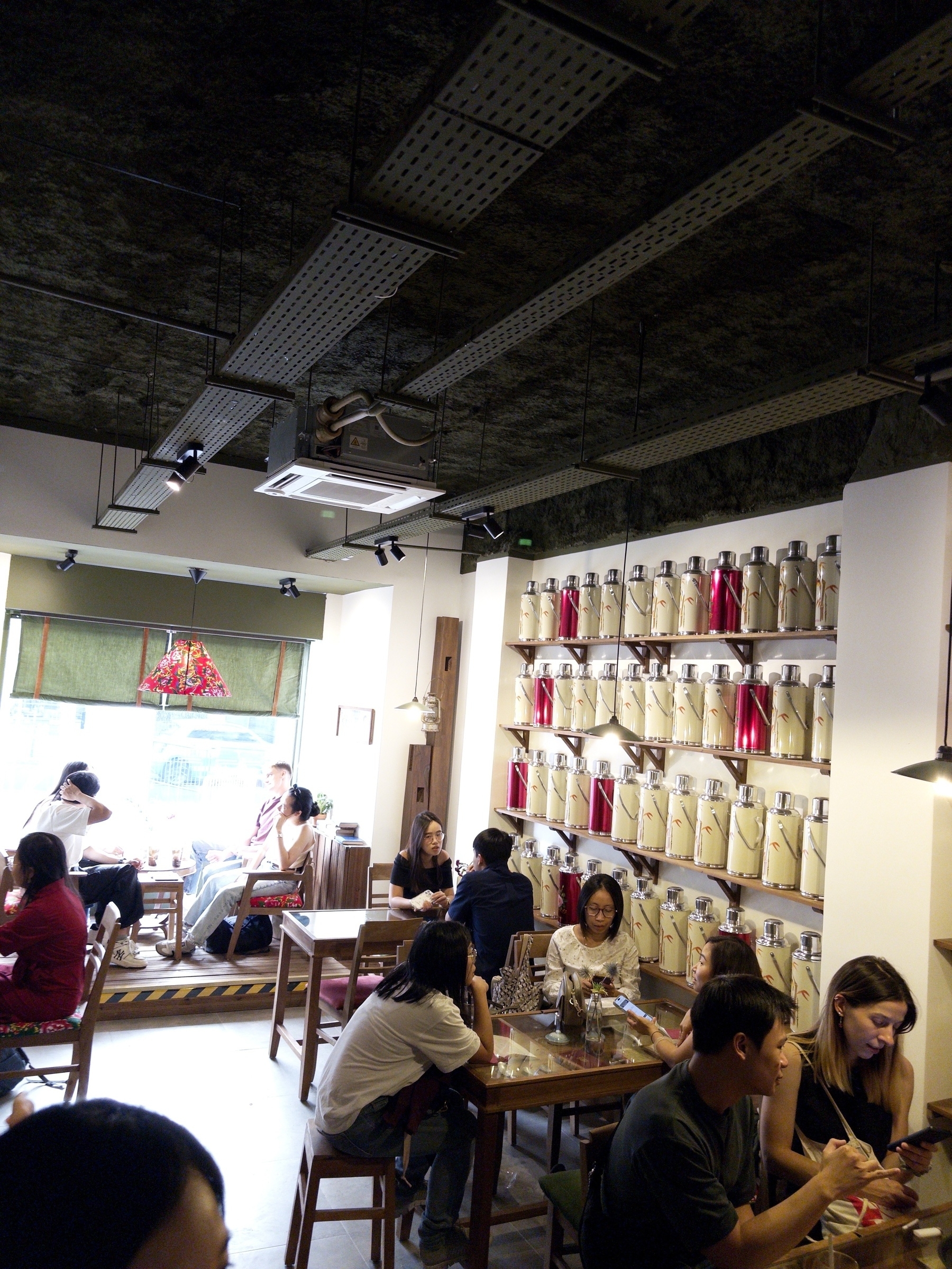 A cozy café scene features people sitting at tables, engaging in conversation, with a wall decorated with colorful teapots.