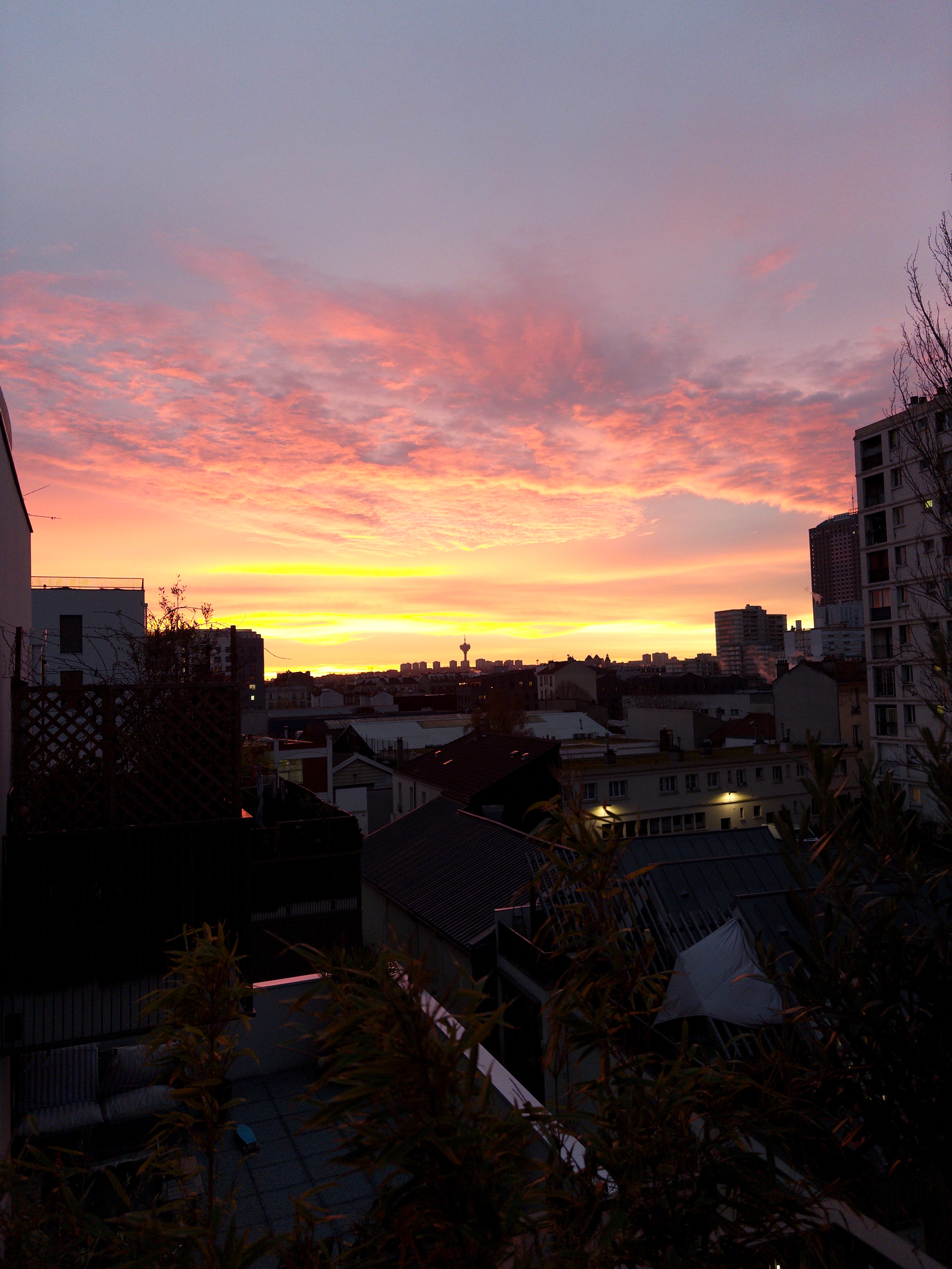 A vibrant sunrise with pink and orange hues lights up the sky over an urban landscape with buildings silhouetted in the foreground.