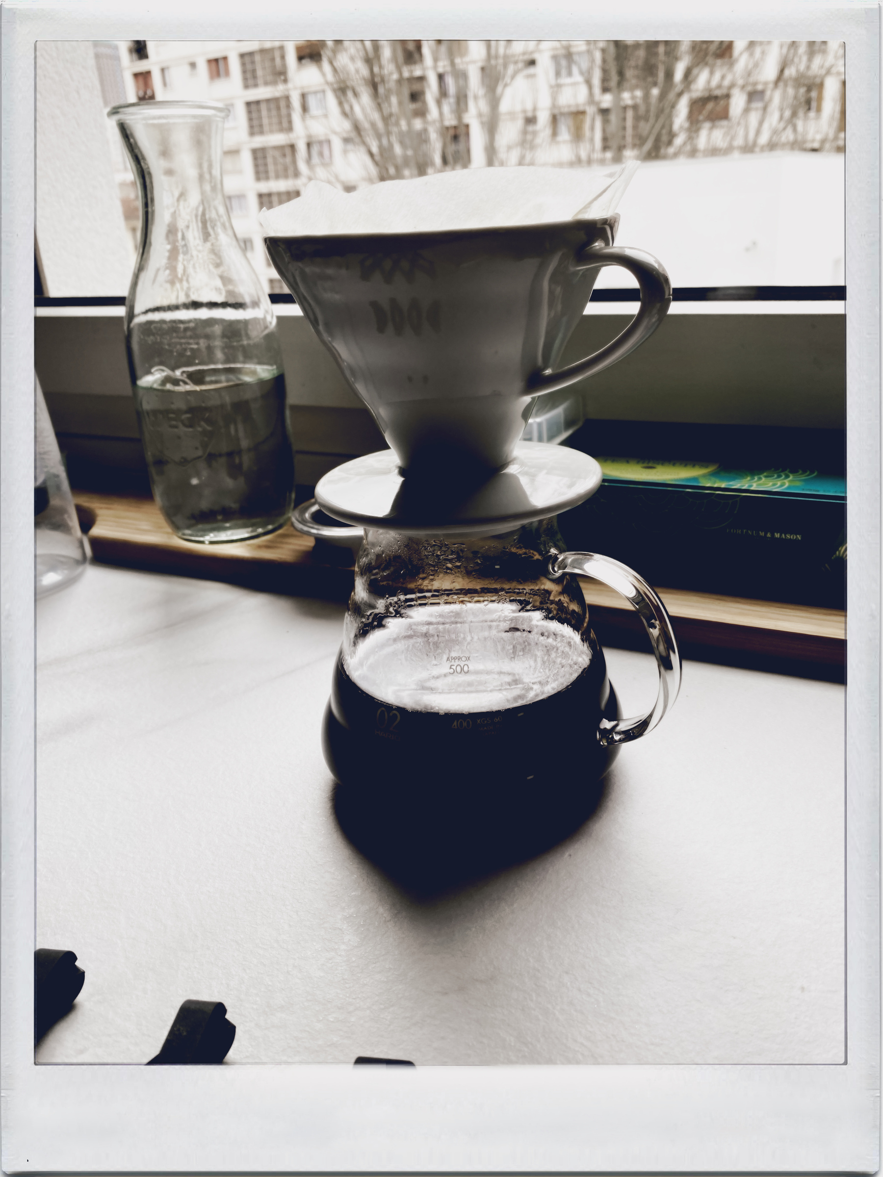 Auto-generated description: A coffee brewing setup featuring a ceramic dripper over a glass carafe is shown by a window.