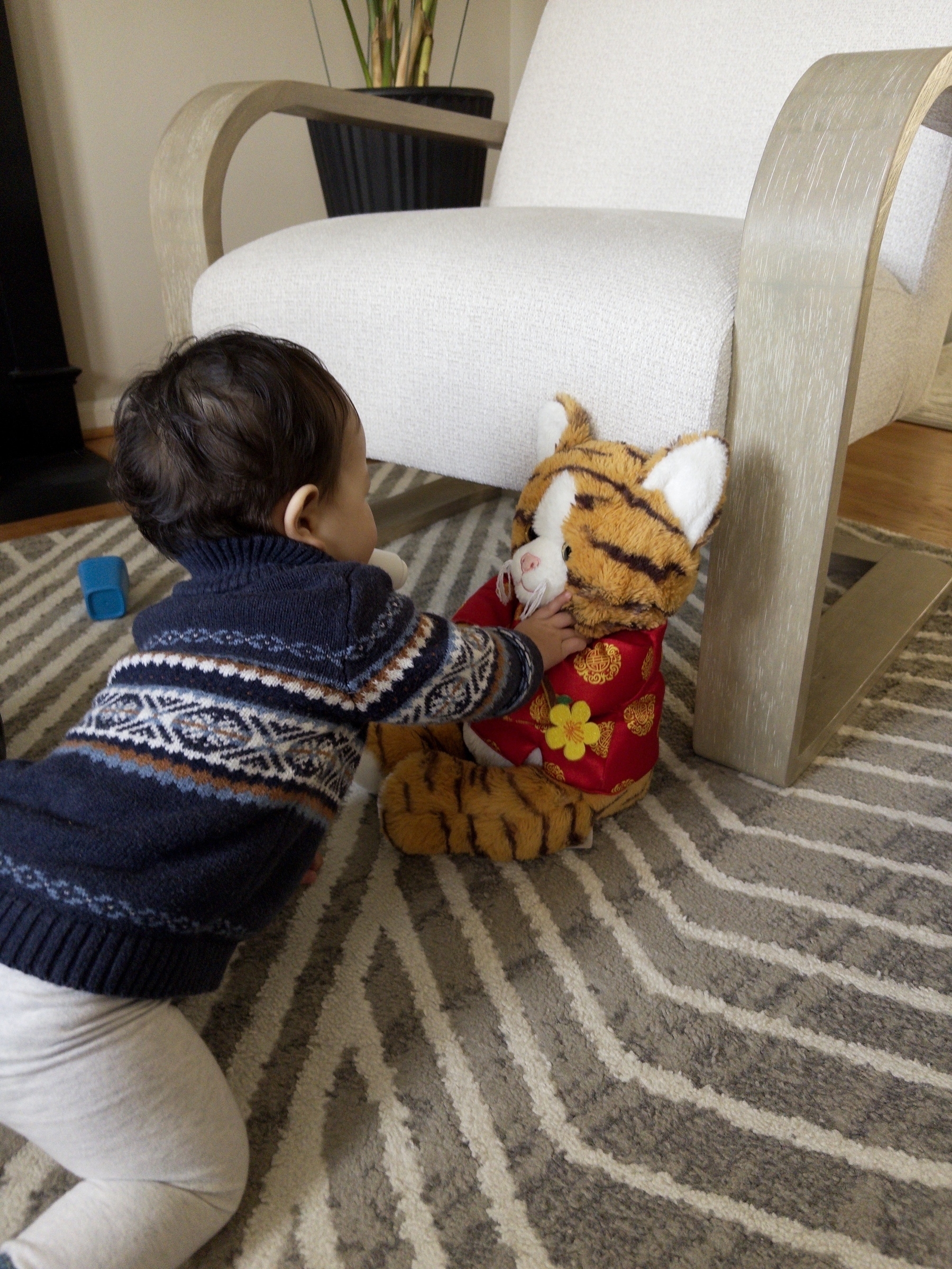 A child is playing with a stuffed animal dressed in a colorful outfit on a patterned carpet.