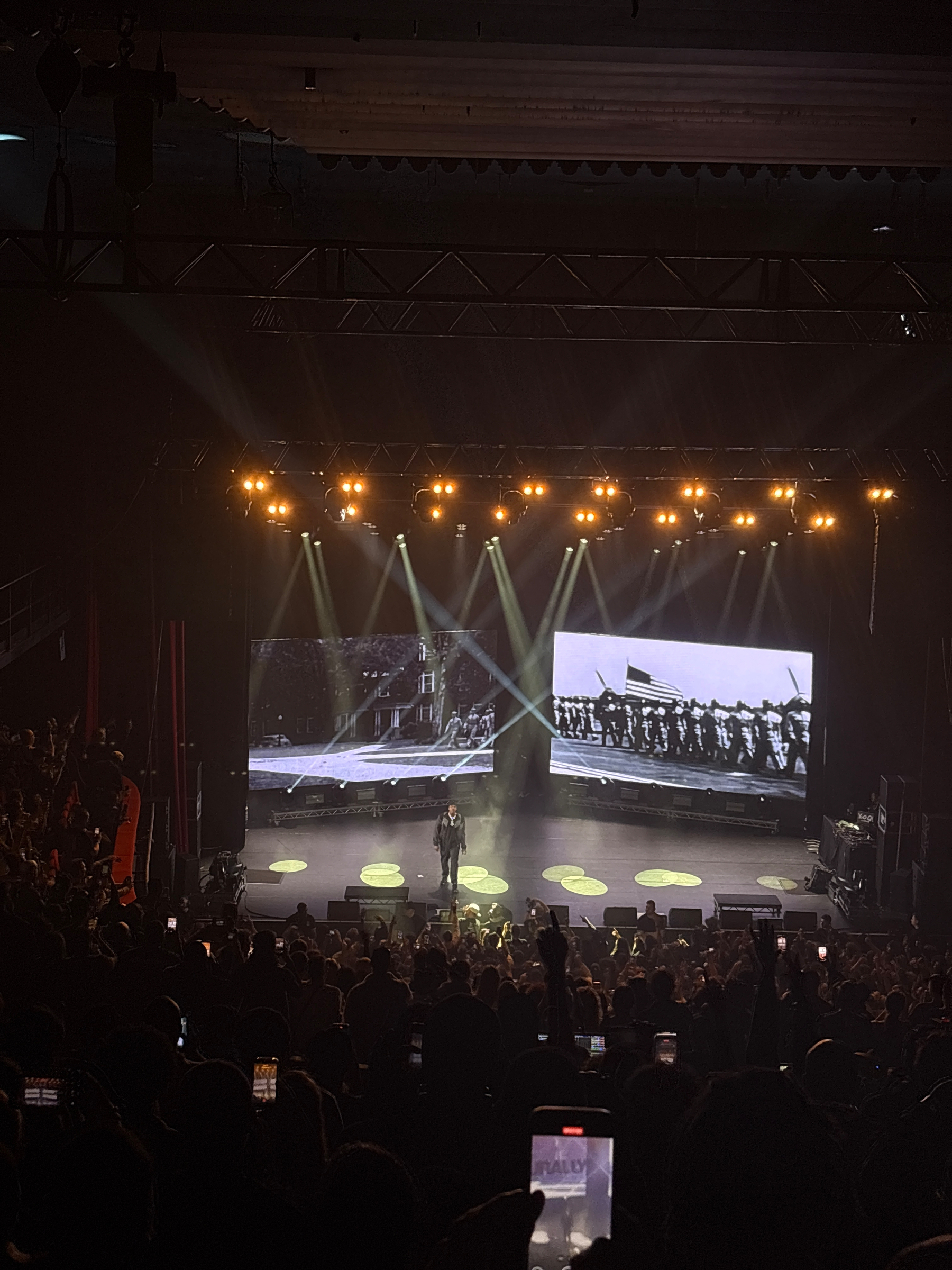 A dimly lit stage features musicians performing in front of large video screens displaying vivid graphics.