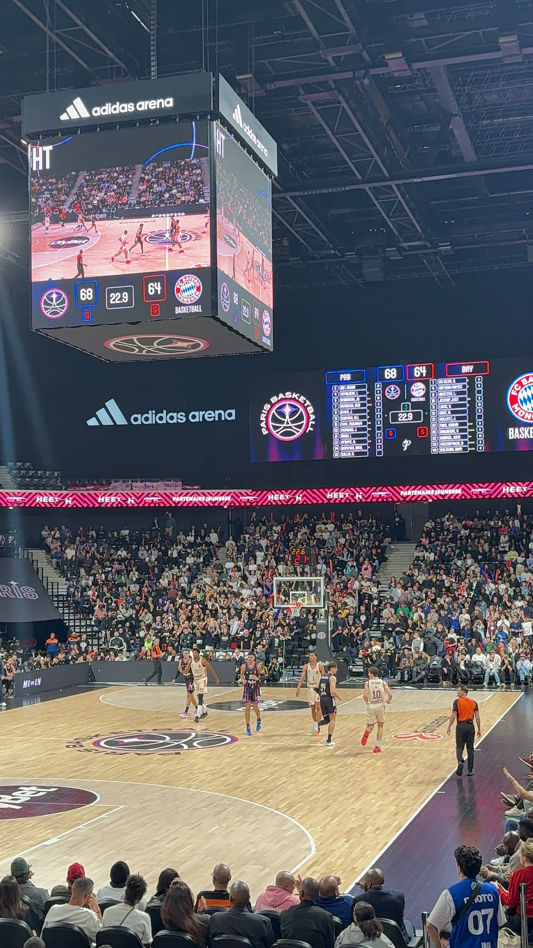 A basketball game is taking place in a large arena with a scoreboard displaying the score and a crowd watching.