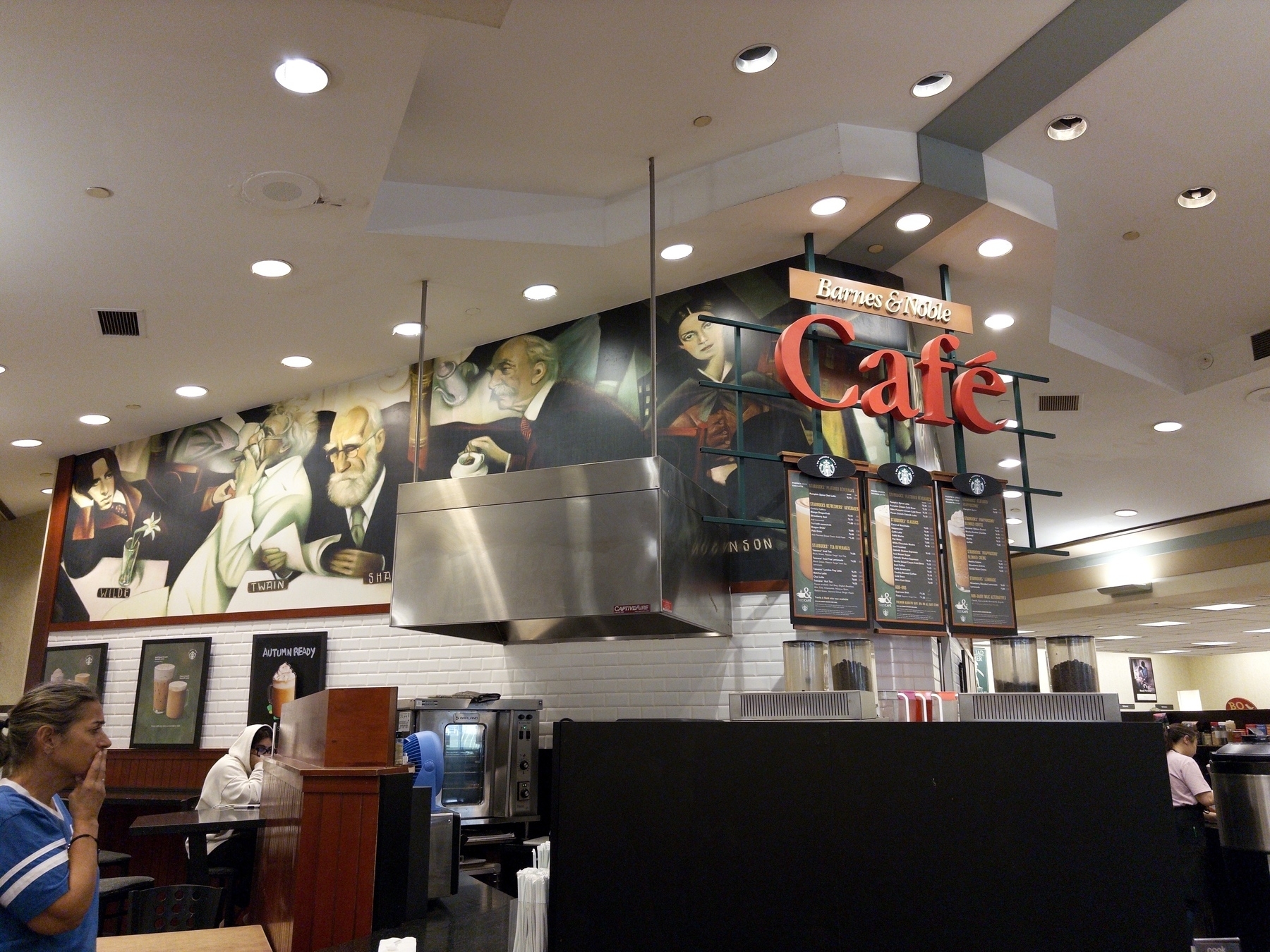 A café with a mural featuring portraits above the counter and a display menu.
