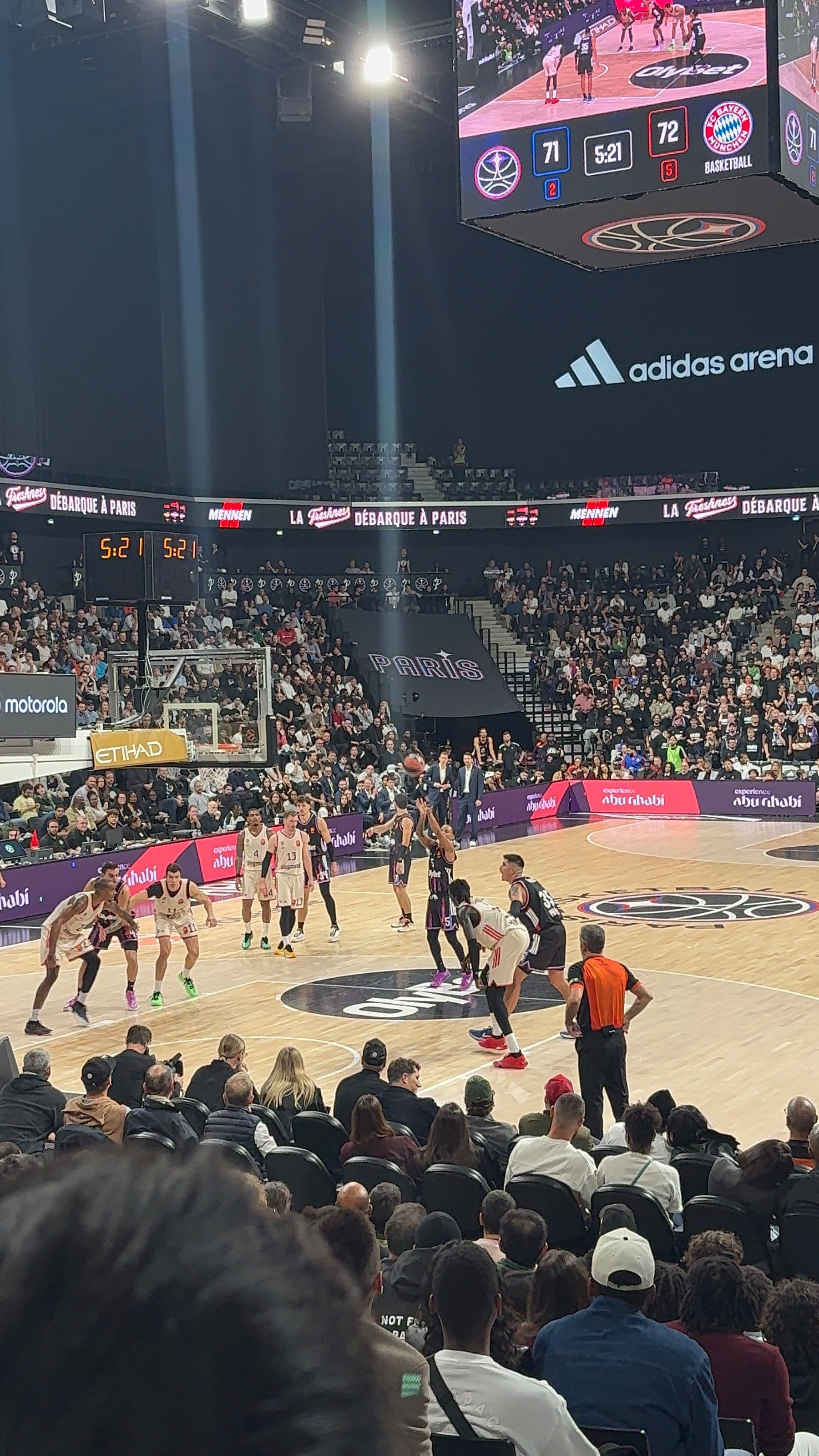 A basketball game is taking place in a crowded arena with players on the court and a scoreboard showing the current score and time remaining.