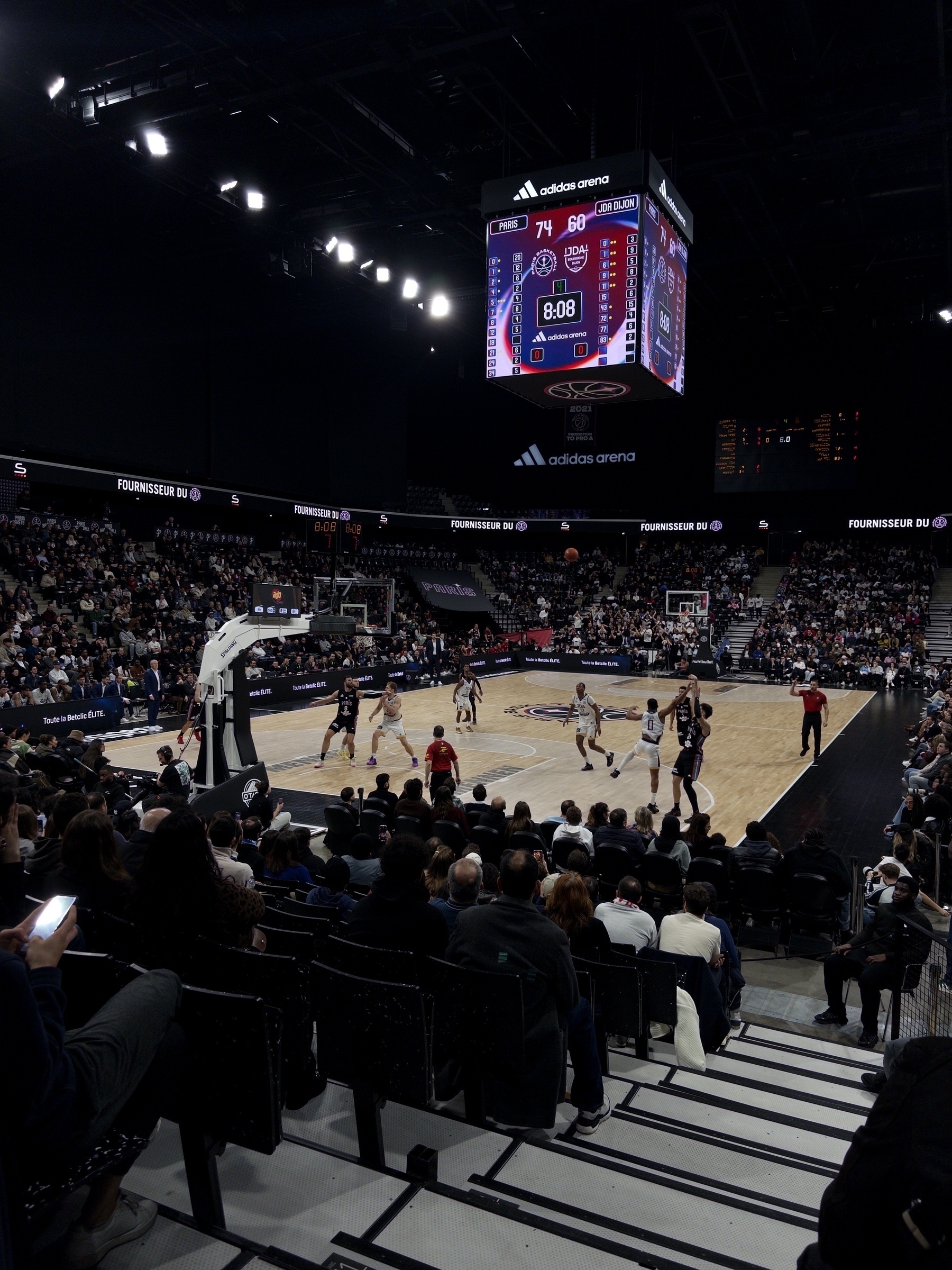 A basketball game is taking place in a packed arena with spectators watching from the stands.