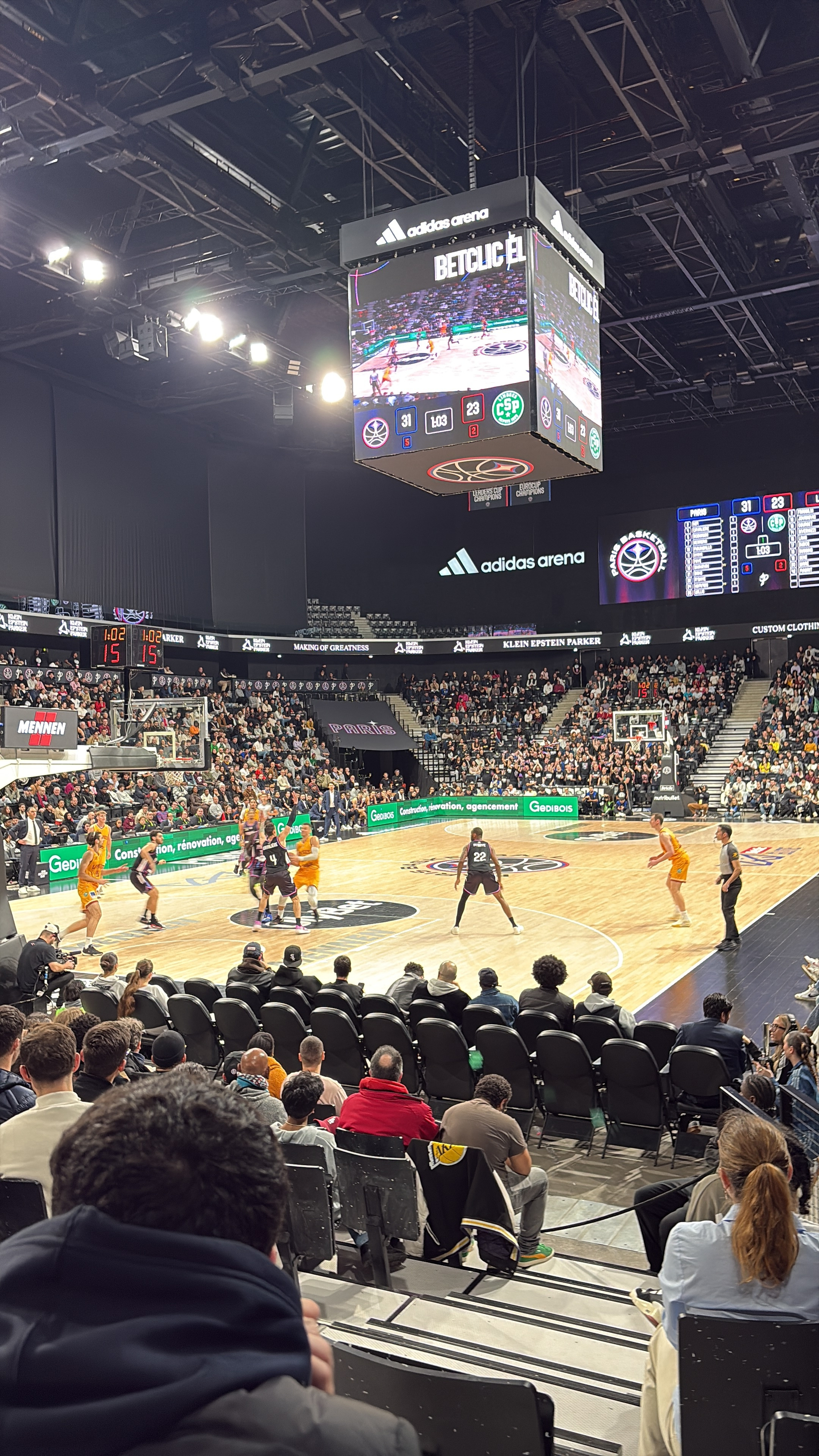 A basketball game is taking place in an indoor arena filled with spectators.